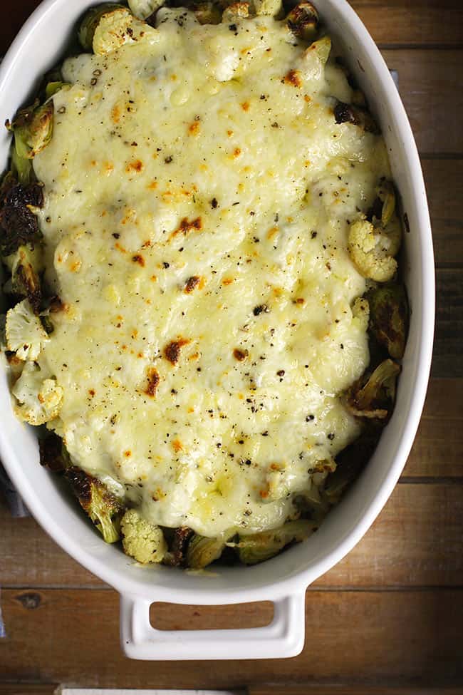 Overhead shot of a casserole dish of roasted Brussels sprouts and cauliflower with gruyere cheese sauce.
