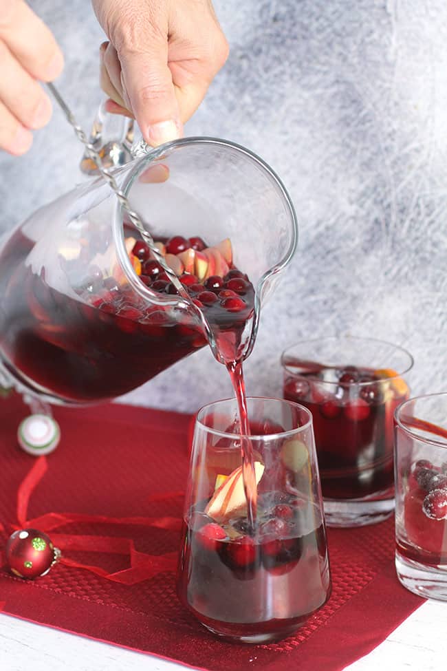 Hands pouring some cranberry sangria into a glass.