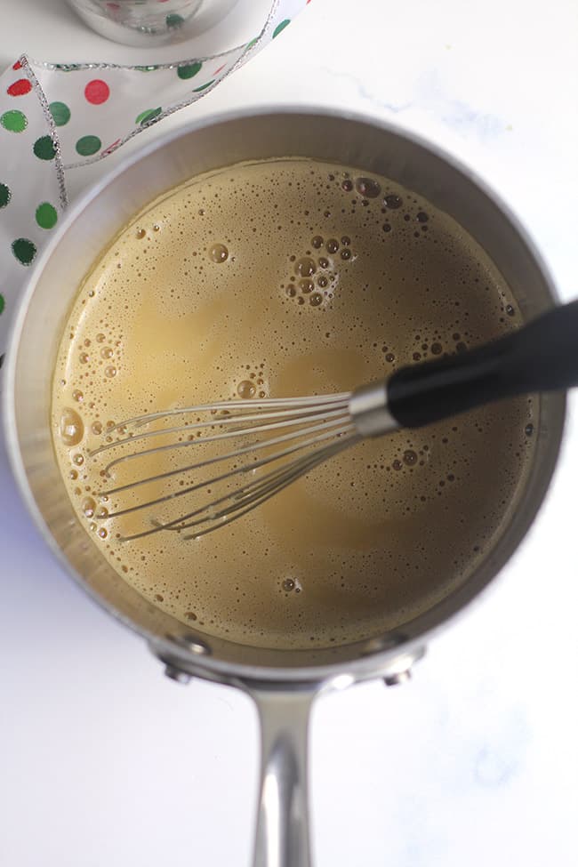 A saucepan of the eggnog lattes with a whisk.
