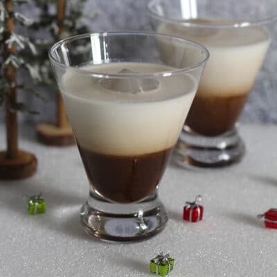 Side shot of two glasses of White Russian cocktails, on a white surface.
