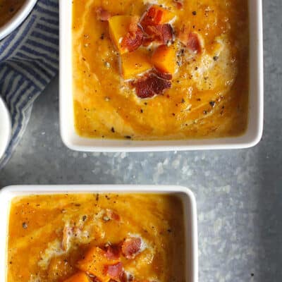 Two square white bowls of butternut squash soup with bacon.