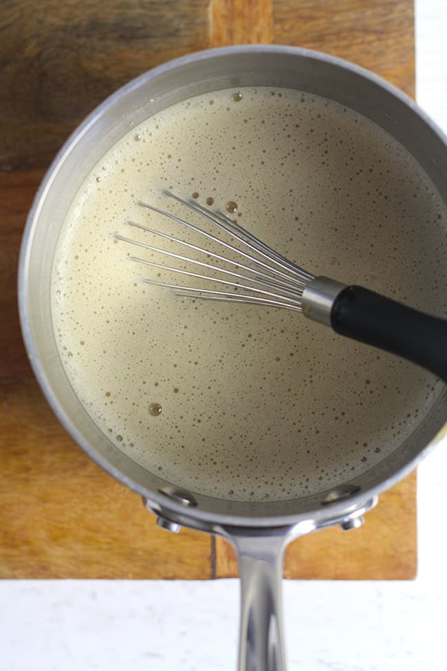 A small saucepan with latte mixture and a whisk inside.
