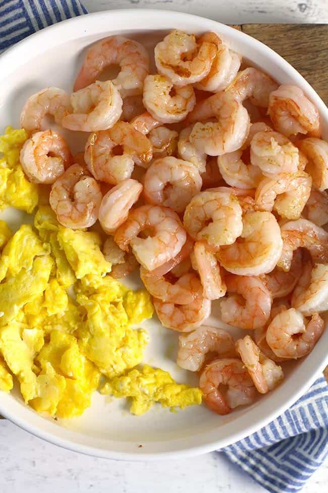A white bowl with the cooked shrimp and the scrambled eggs.