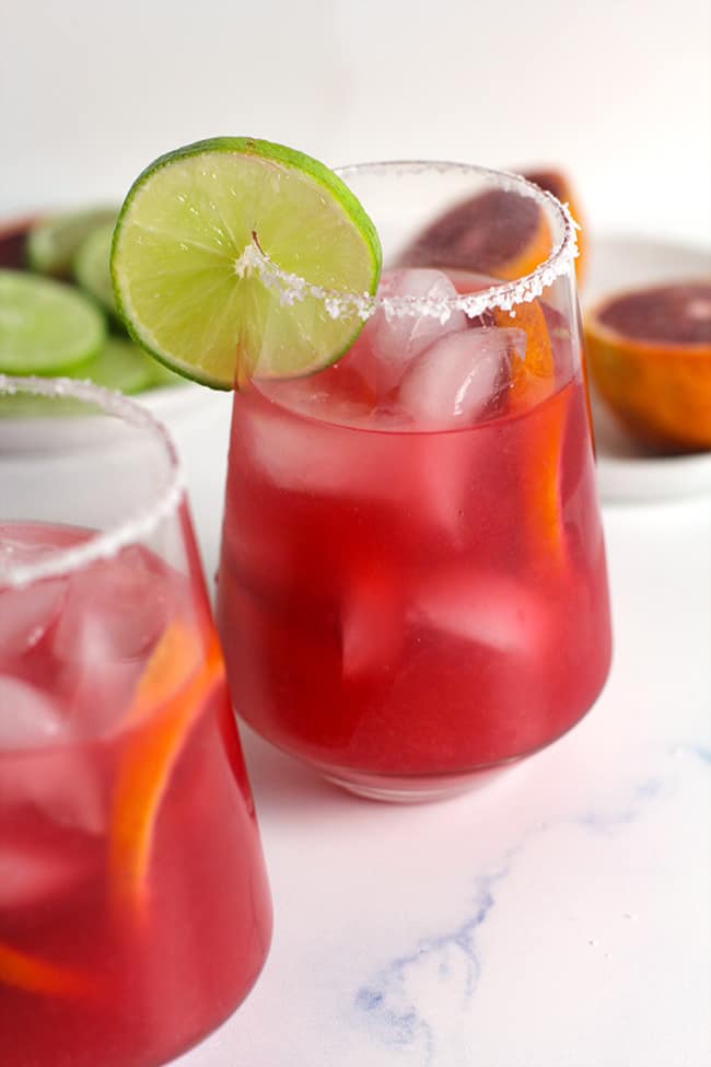 Two blood orange margaritas with salty rims plus lime slices.