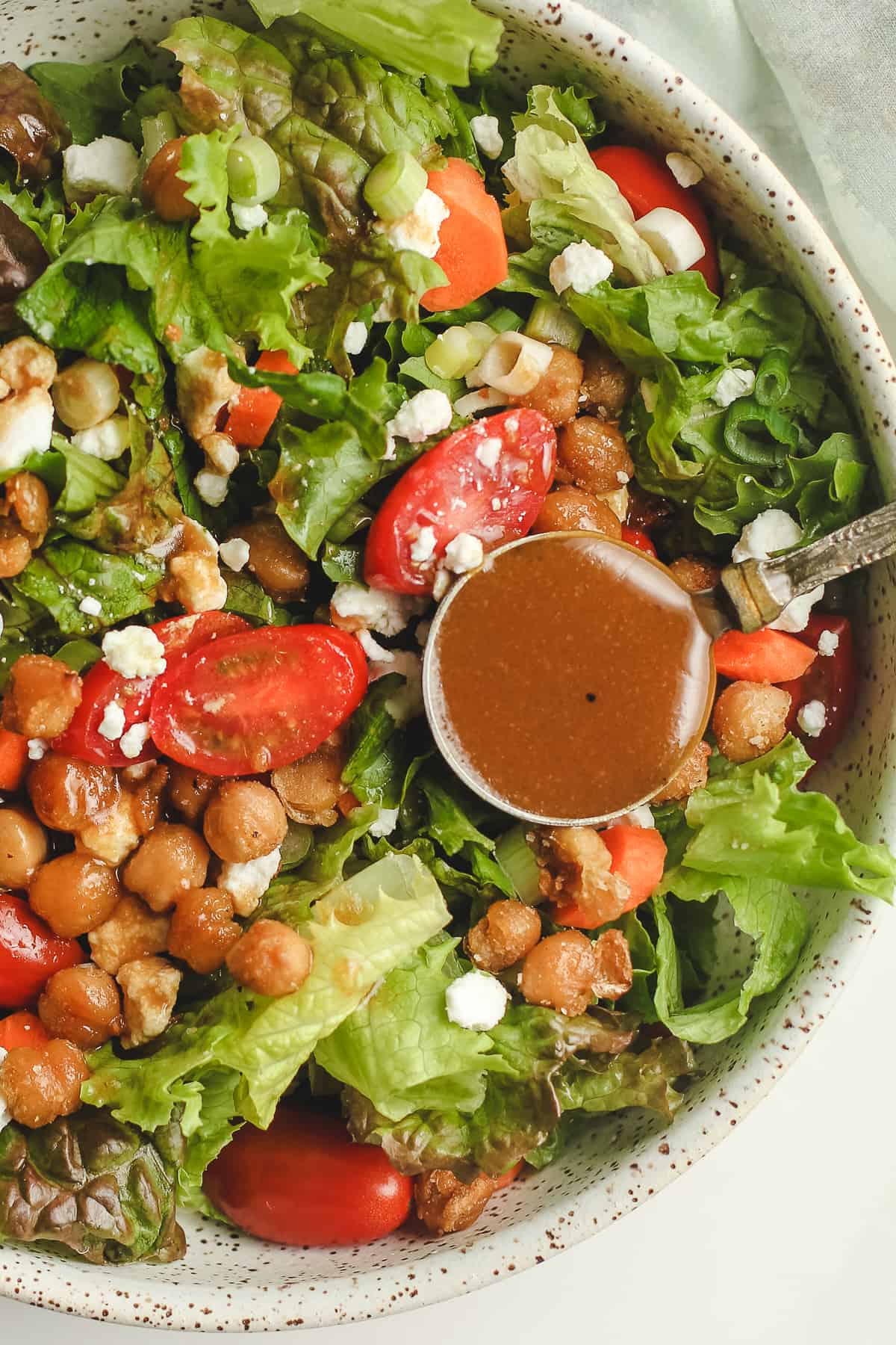 A closeup of a green salad with a spoonful of balsamic vinaigrette.
