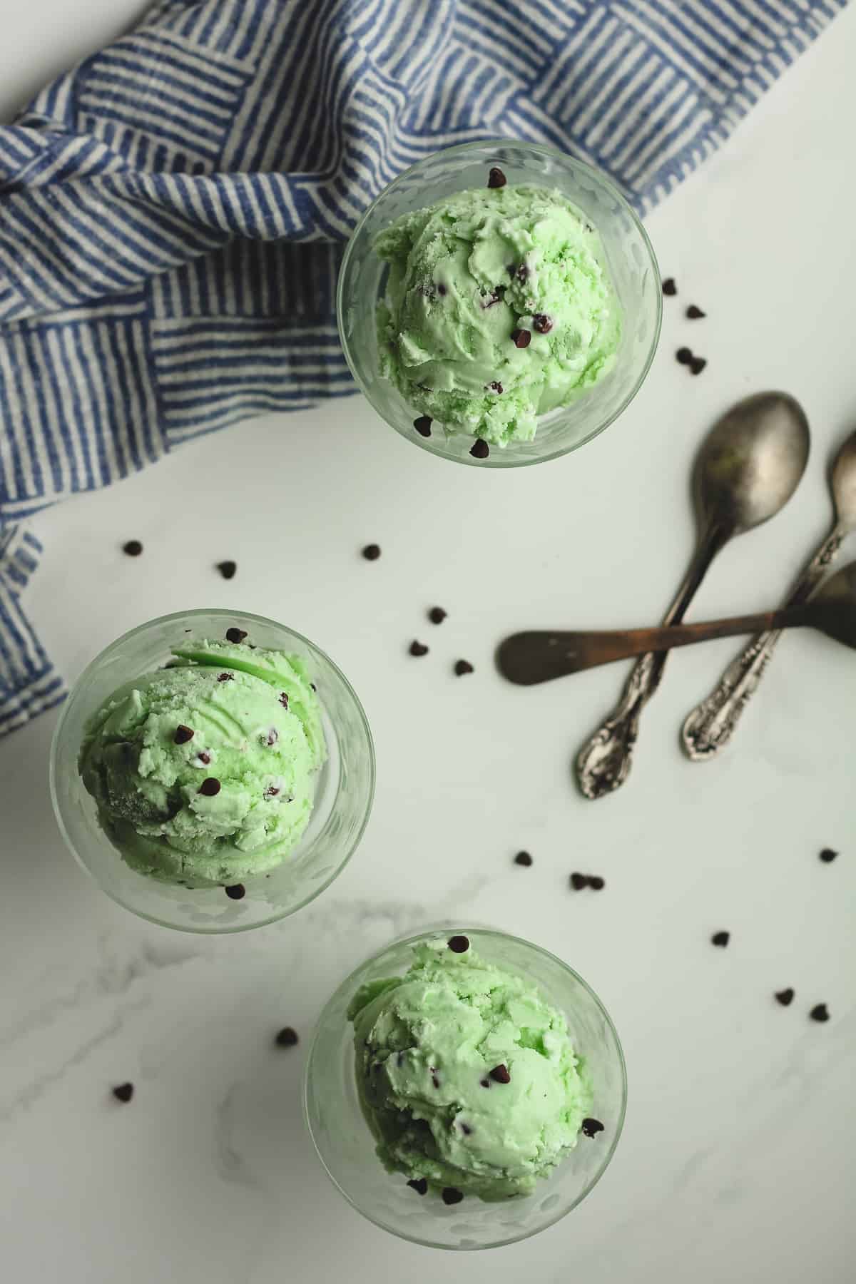 Overhead shot of three small bowls of mint chip ice cream, with spoons.
