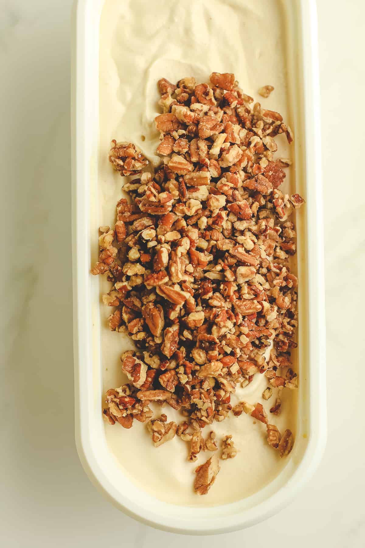 A container of pecan ice cream, with pecans on the top.