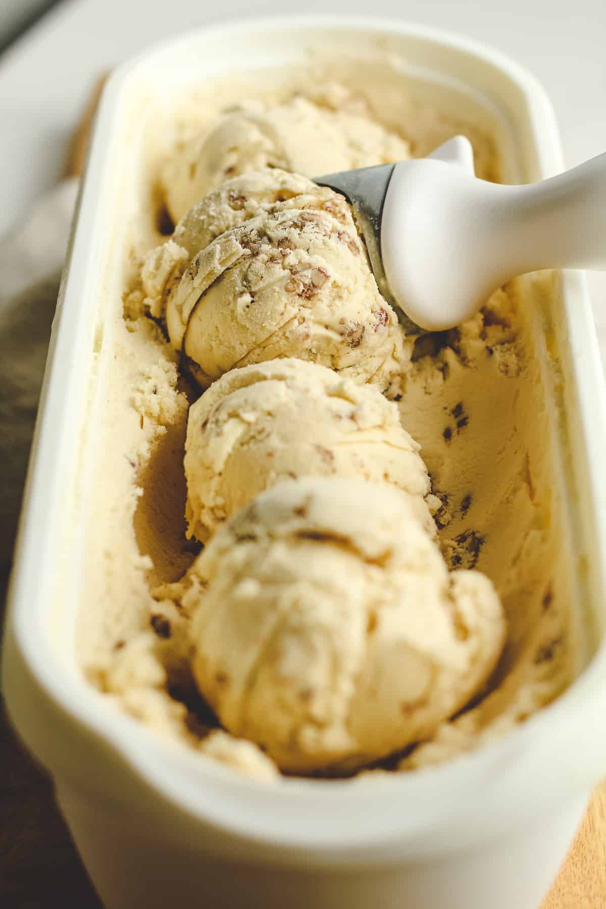 Side shot of a white container of butter pecan ice cream, arranged in scoops.