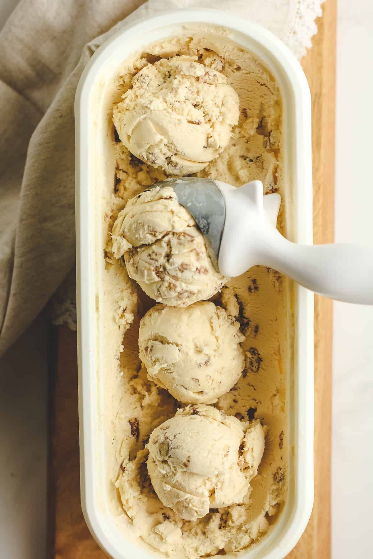 A white container of butter pecan ice cream, arranged in scoops.