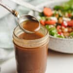Side shot of a jar of honey balsamic vinaigrette, with a salad in the background.