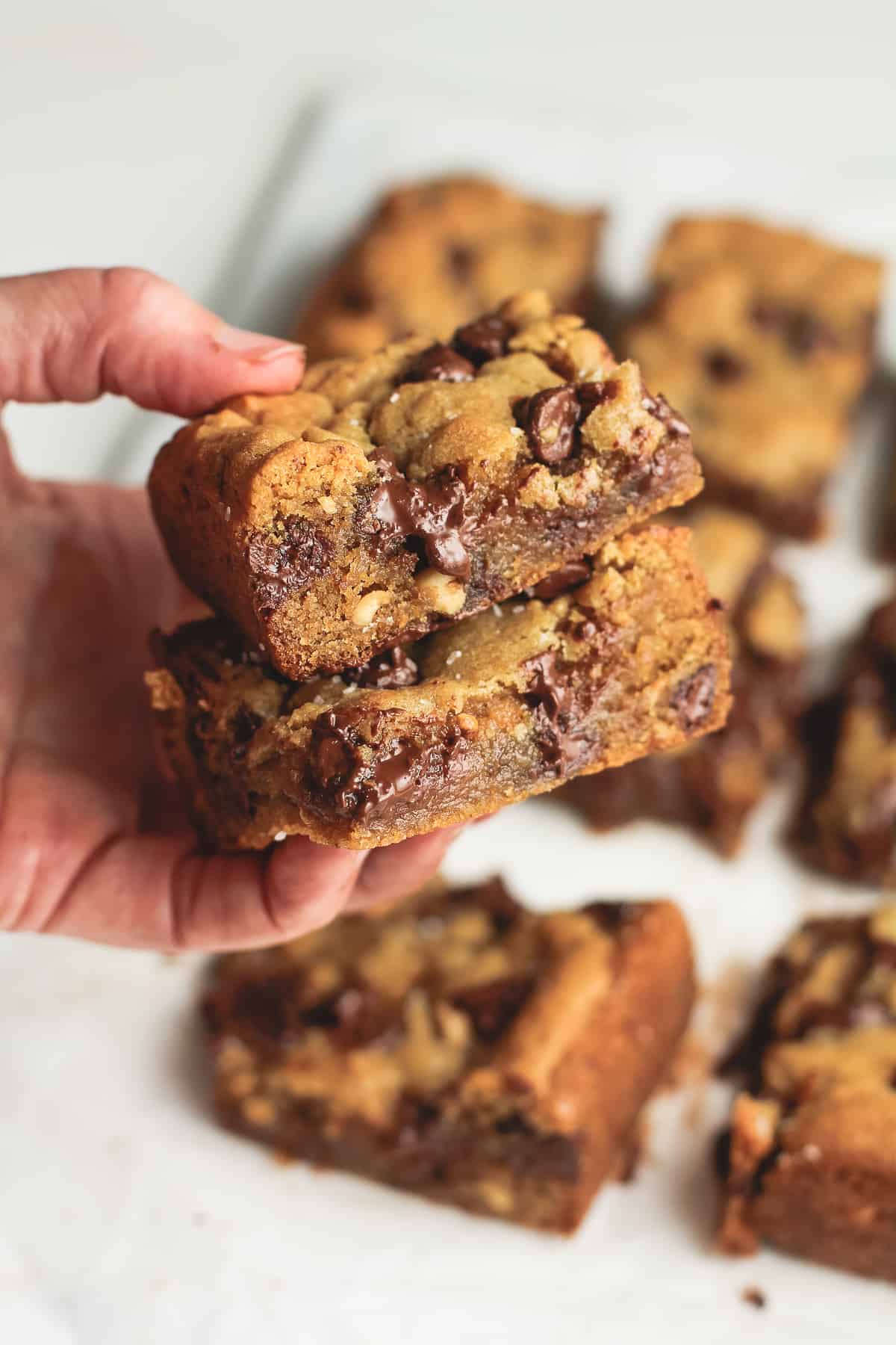 My hand holding two chocolate chip peanut butter blondies.