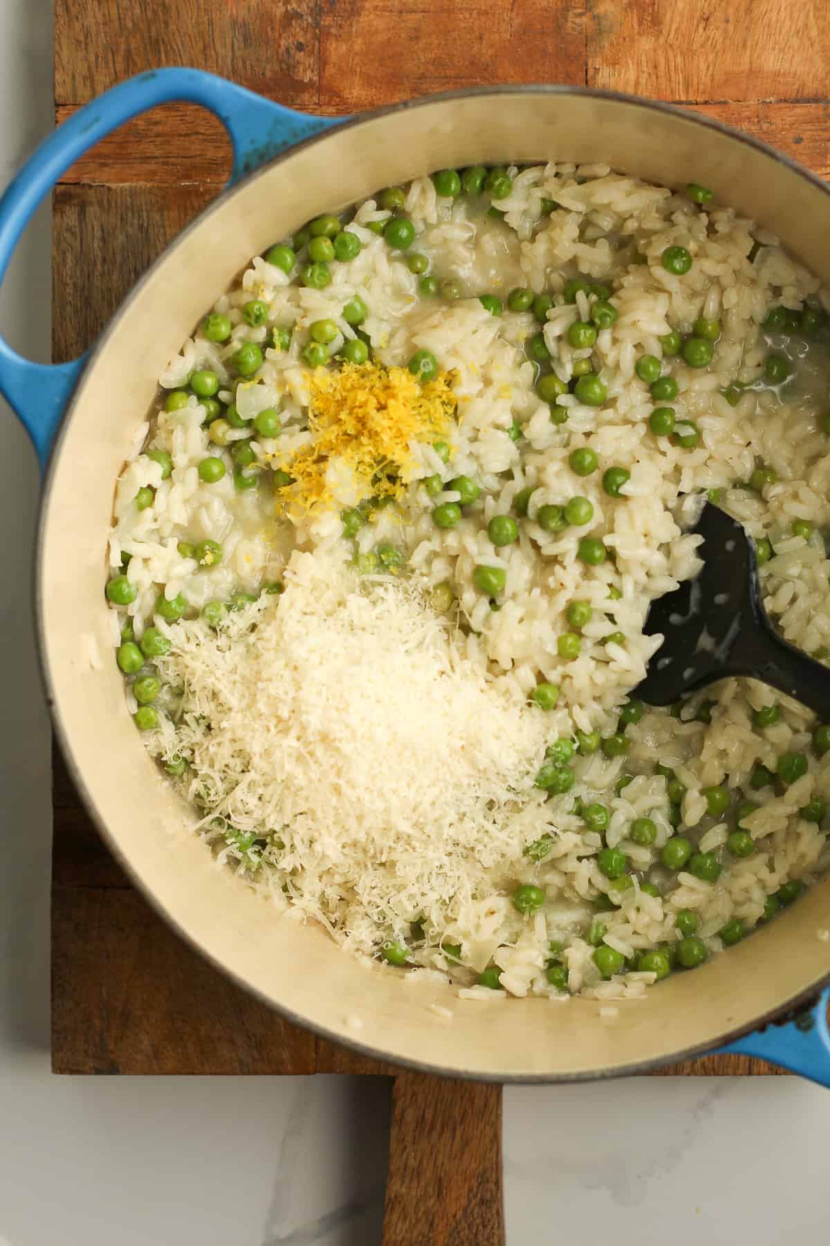 A stock pot of risotto with peas, parmesan cheese, and lemon zest on top.