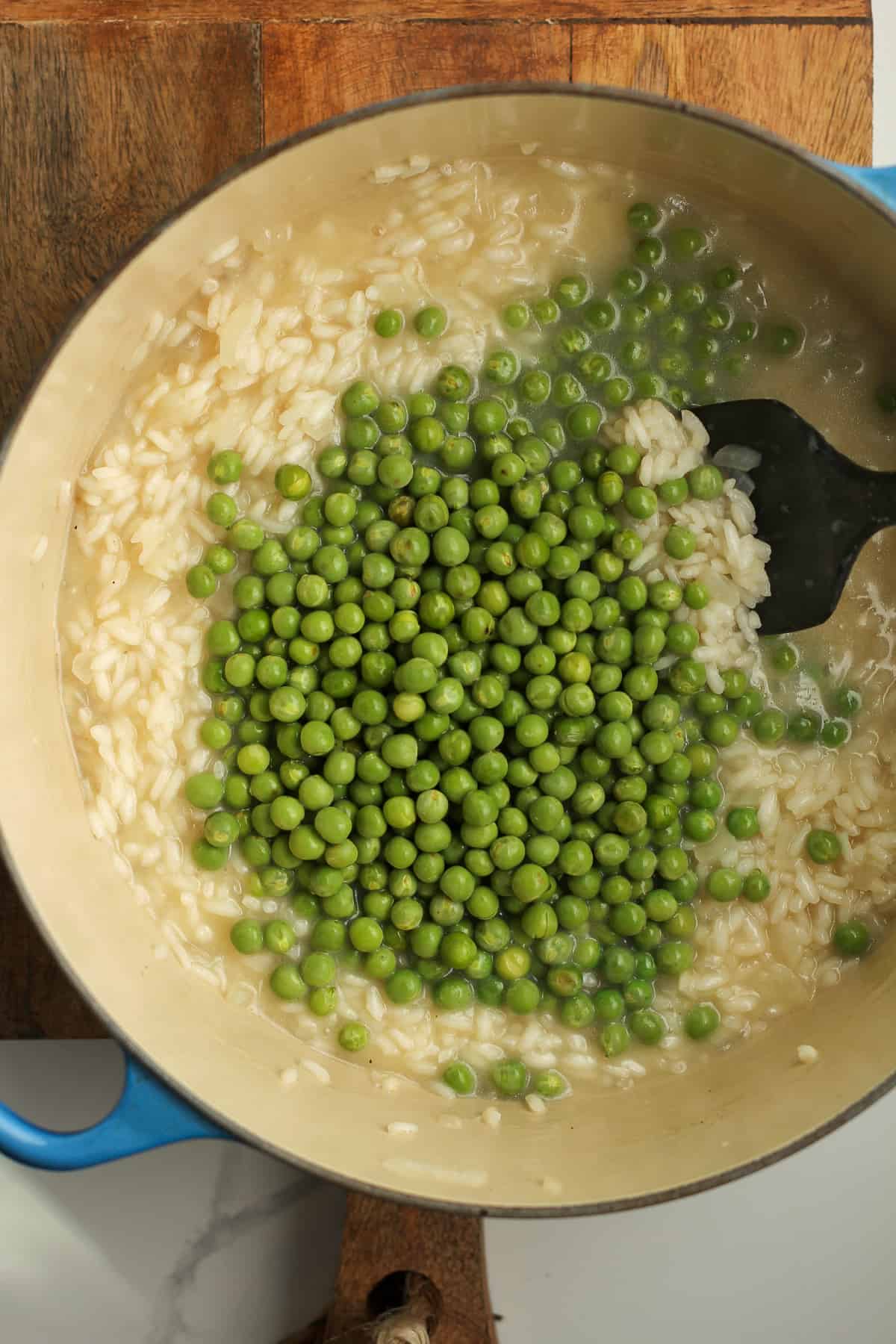 A stock pot of the risotto cooking with peas on top.