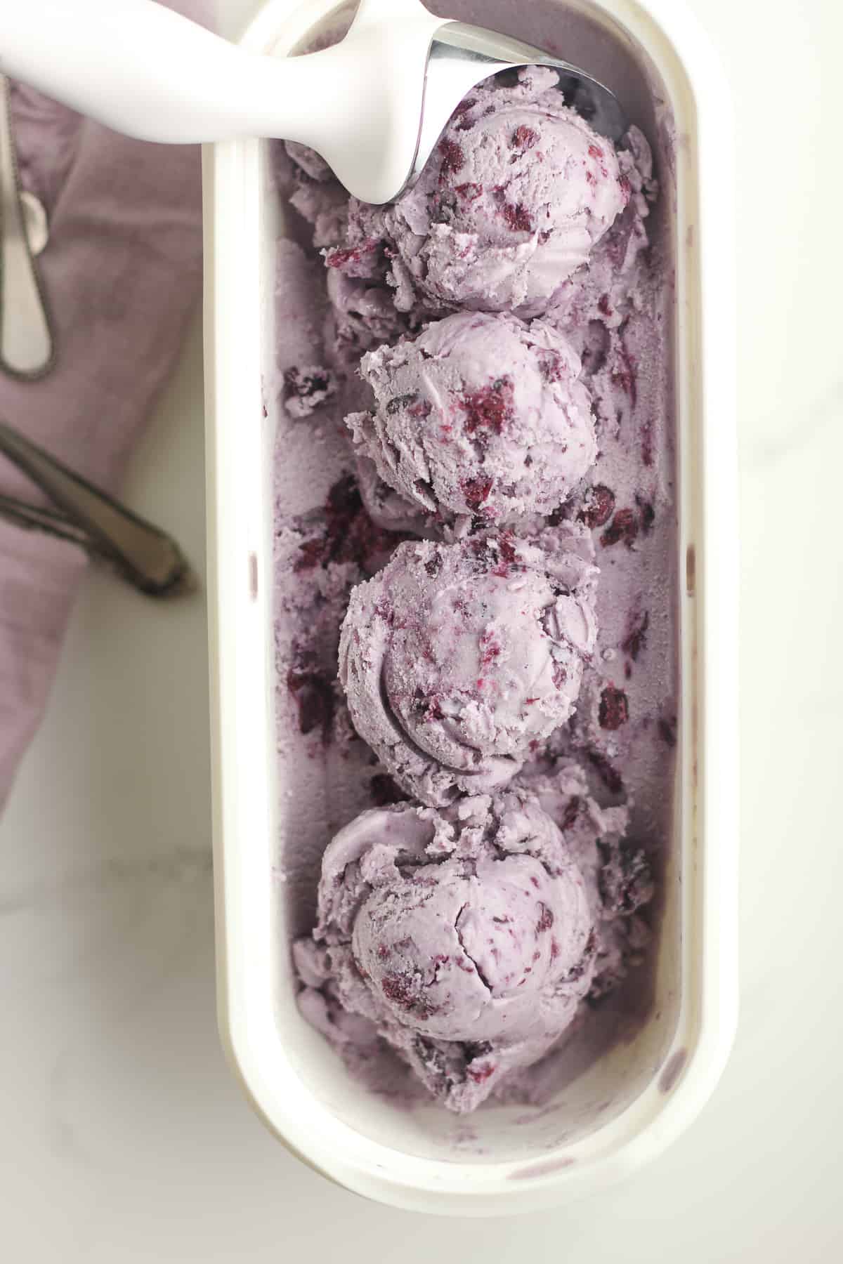 An oblong white container of blueberry ice cream, formed into four scoops.