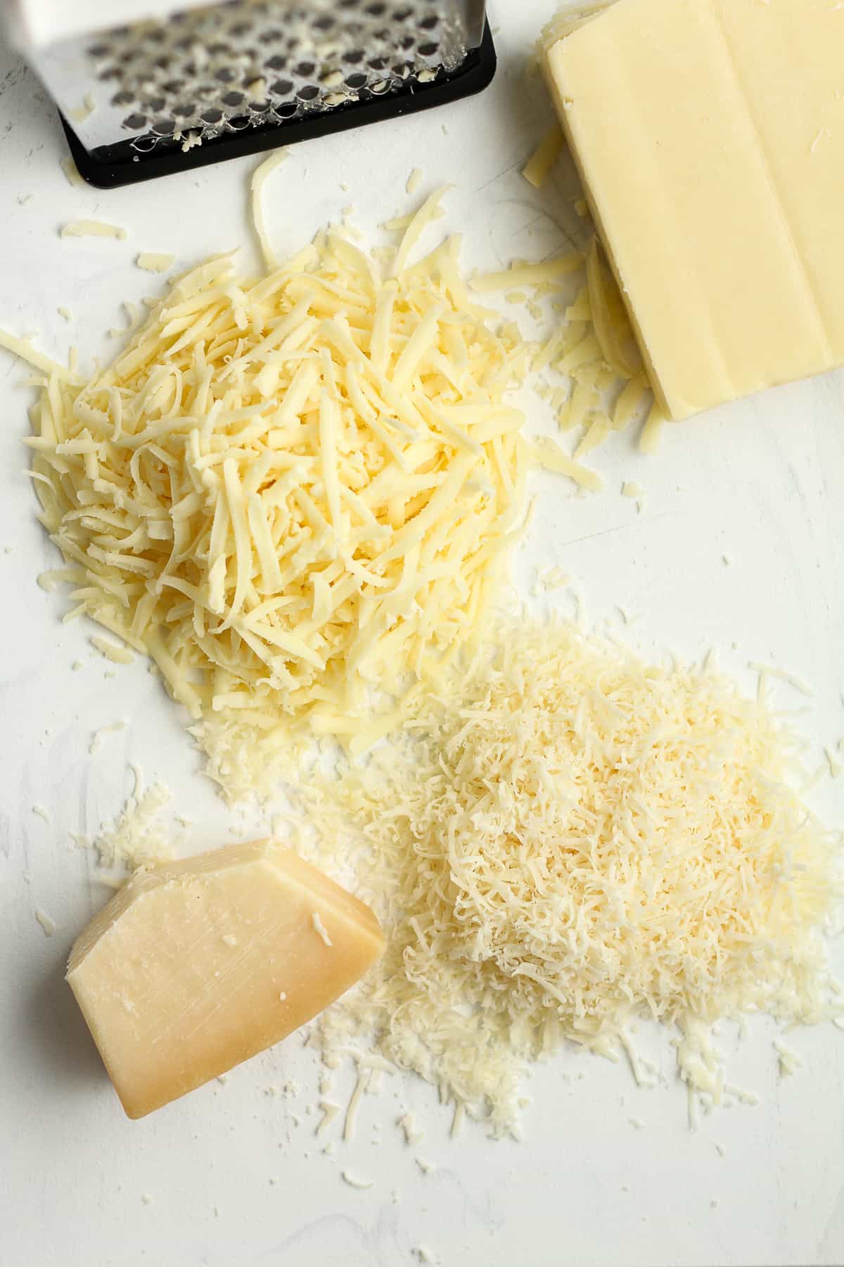 A cutting board of the shredded mozzarella cheese and the shredded parmesan cheese.