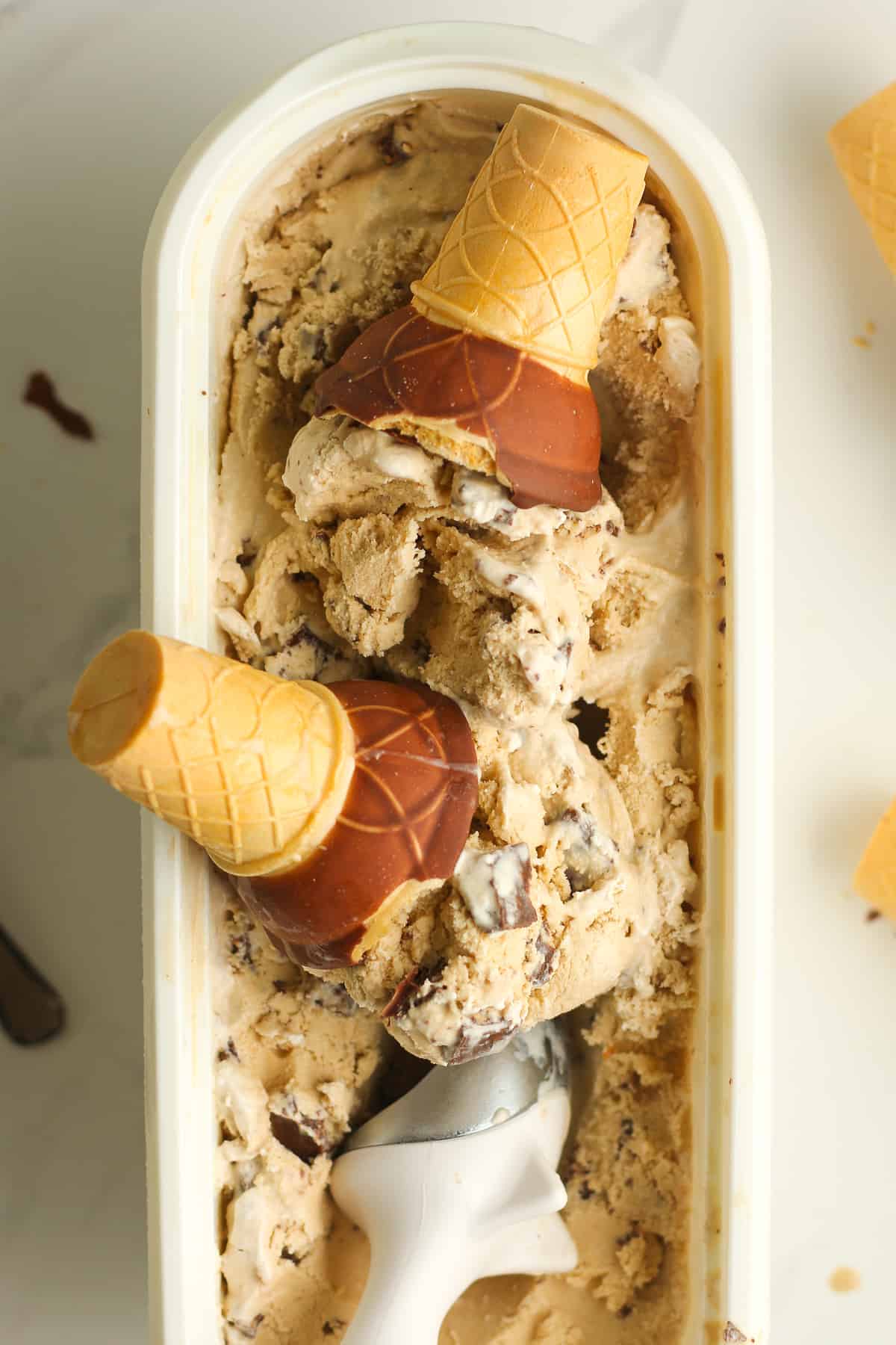 A container of ice cream, with cones dipped in it.