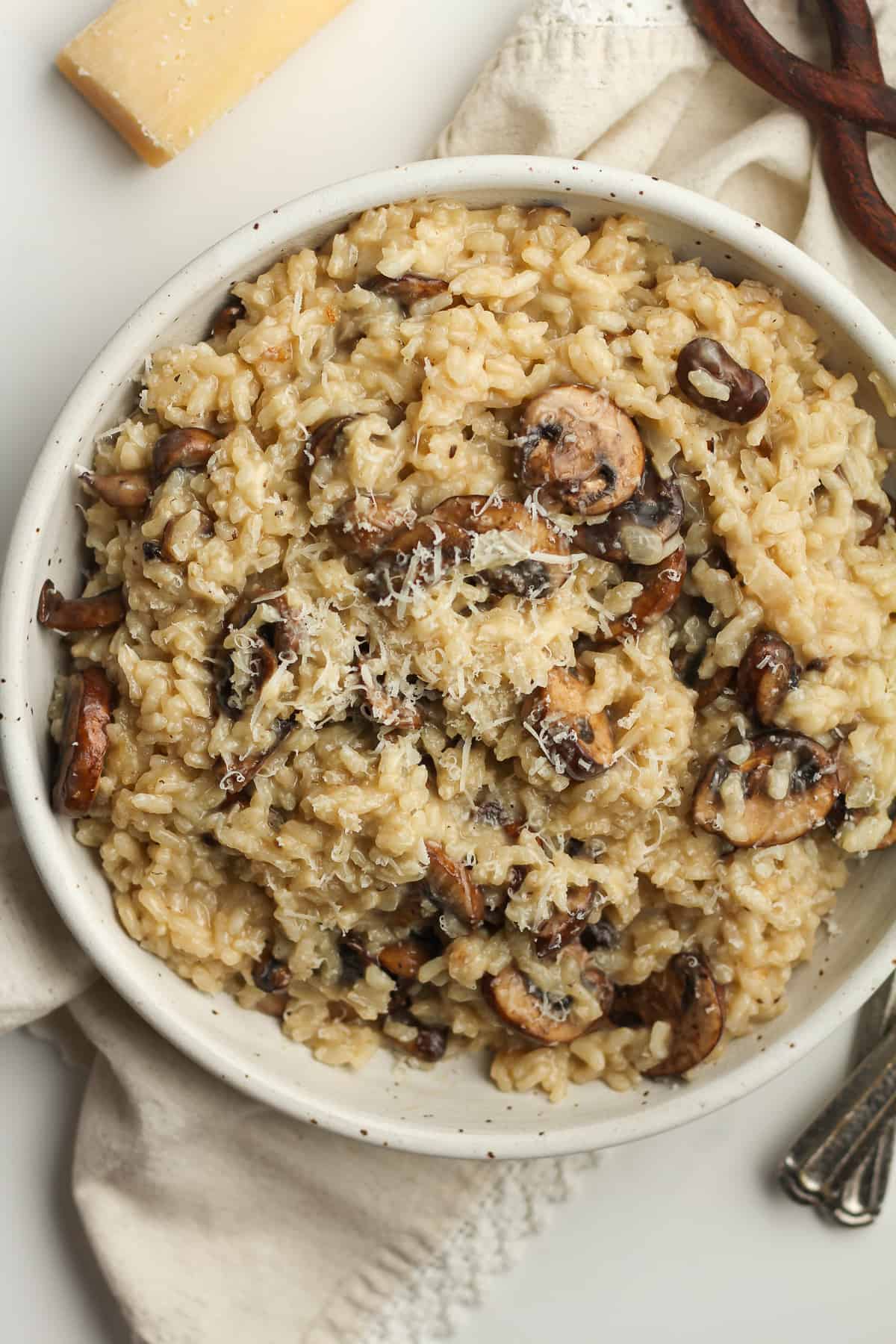 Overhead shot of a bowl of mushroom risotto, with a wedge of parmesan cheese.