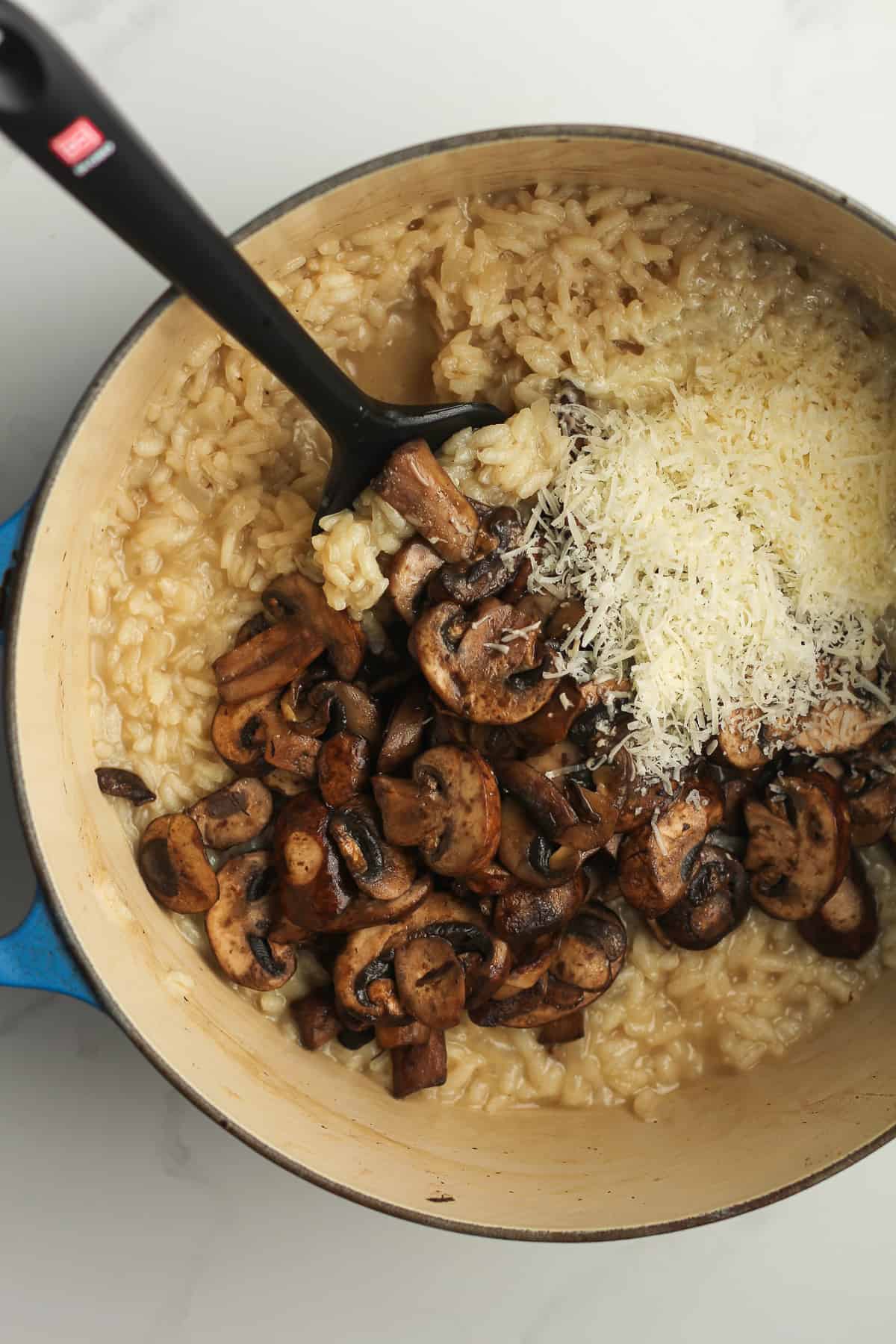A stock pot of mushroom risotto, with mushrooms and parmesan cheese on top.