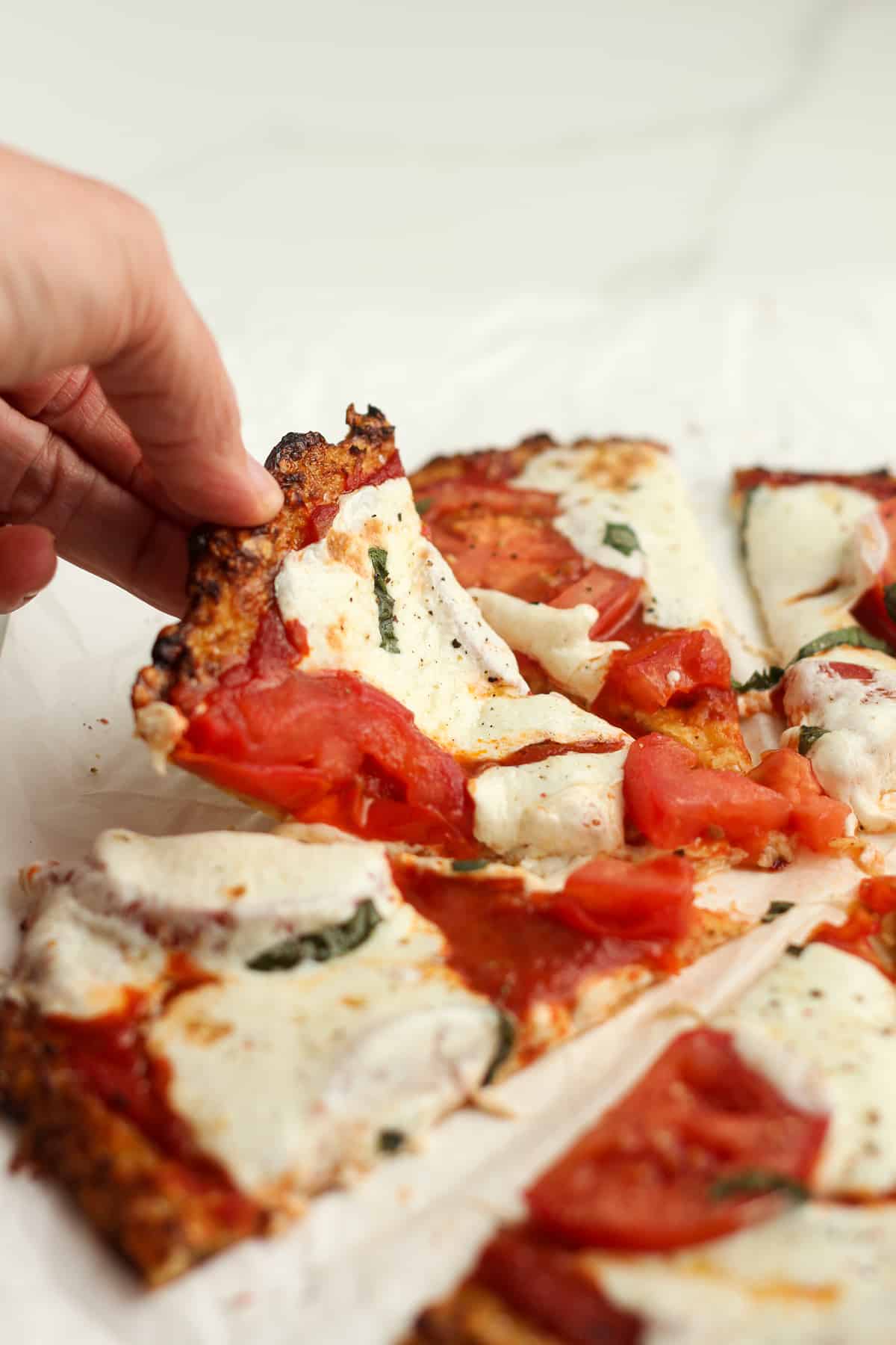Side shot of a hand picking up a piece of Margherita pizza on cauliflower crust.