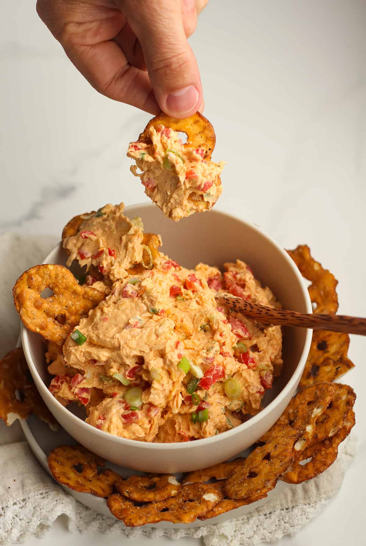 A hand holding a pretzel crisp with pimento cheese on it.