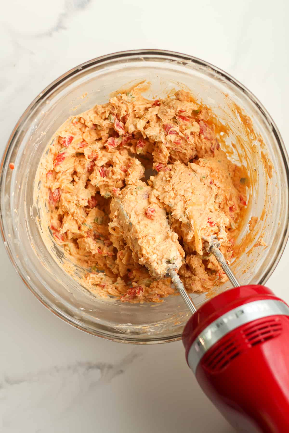 A hand mixer in a bowl of blended pimento cheese.