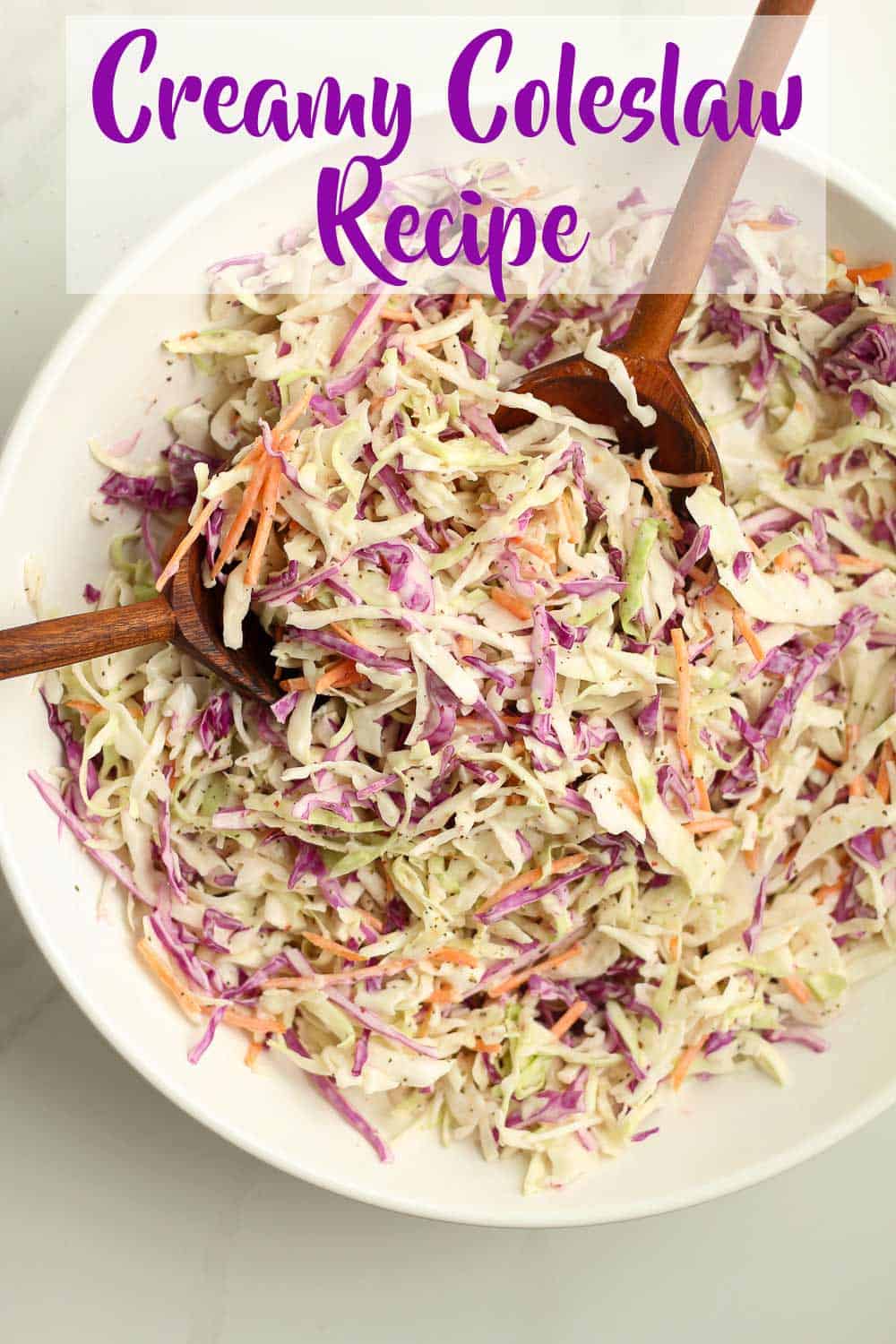 A large bowl of creamy coleslaw with wooden spoons.