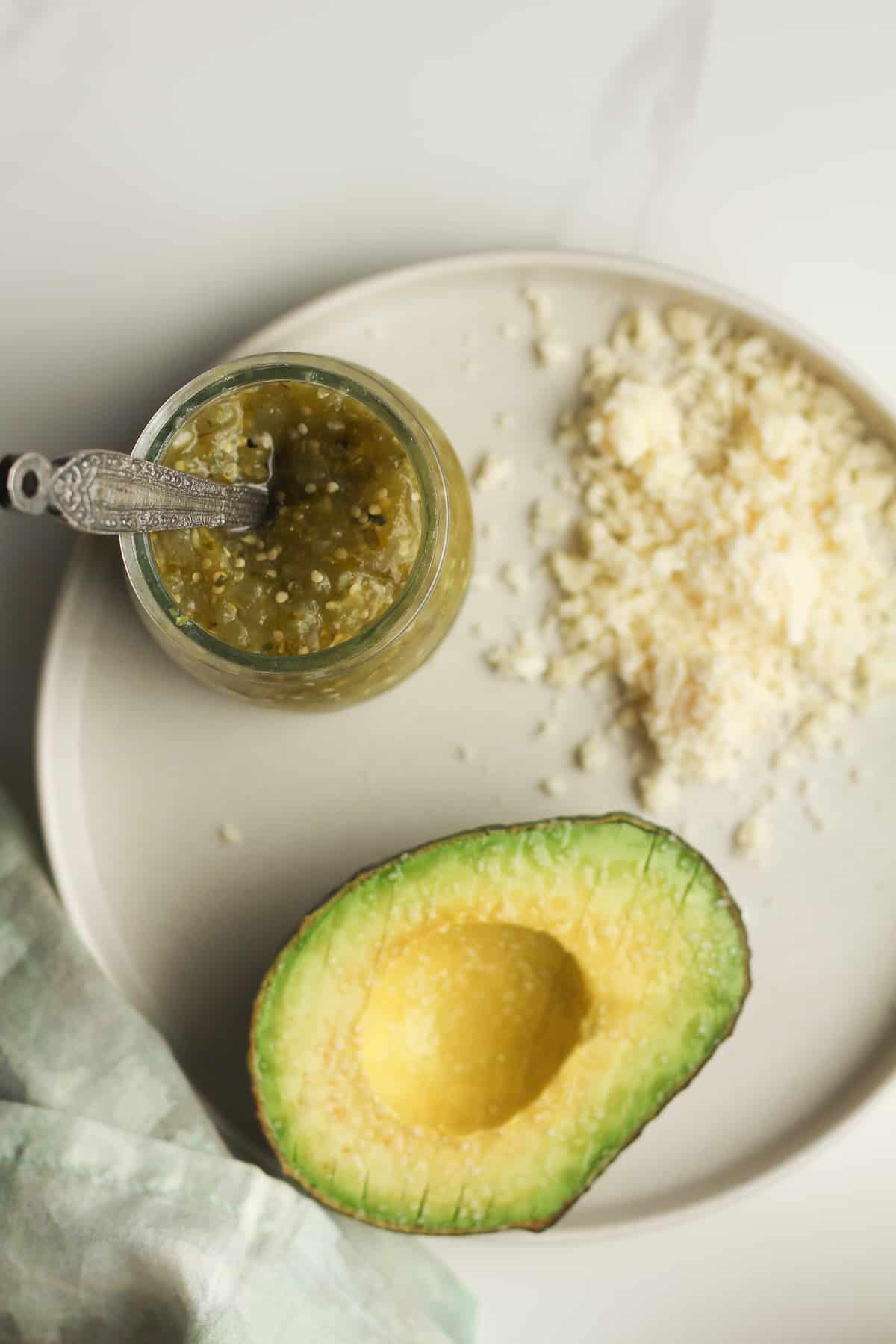A plate of the salsa verde, Cotija cheese, and a sliced half avocado.