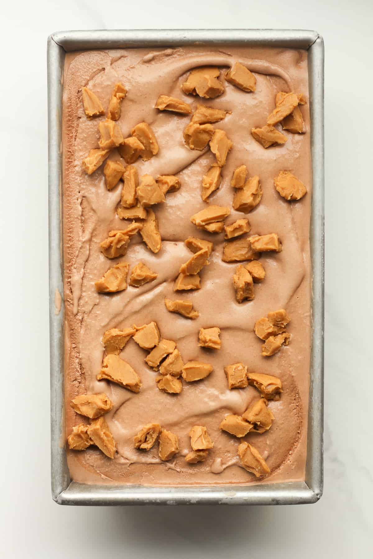 A pan of chocolate peanut butter ice cream with chunks of peanut butter on top.