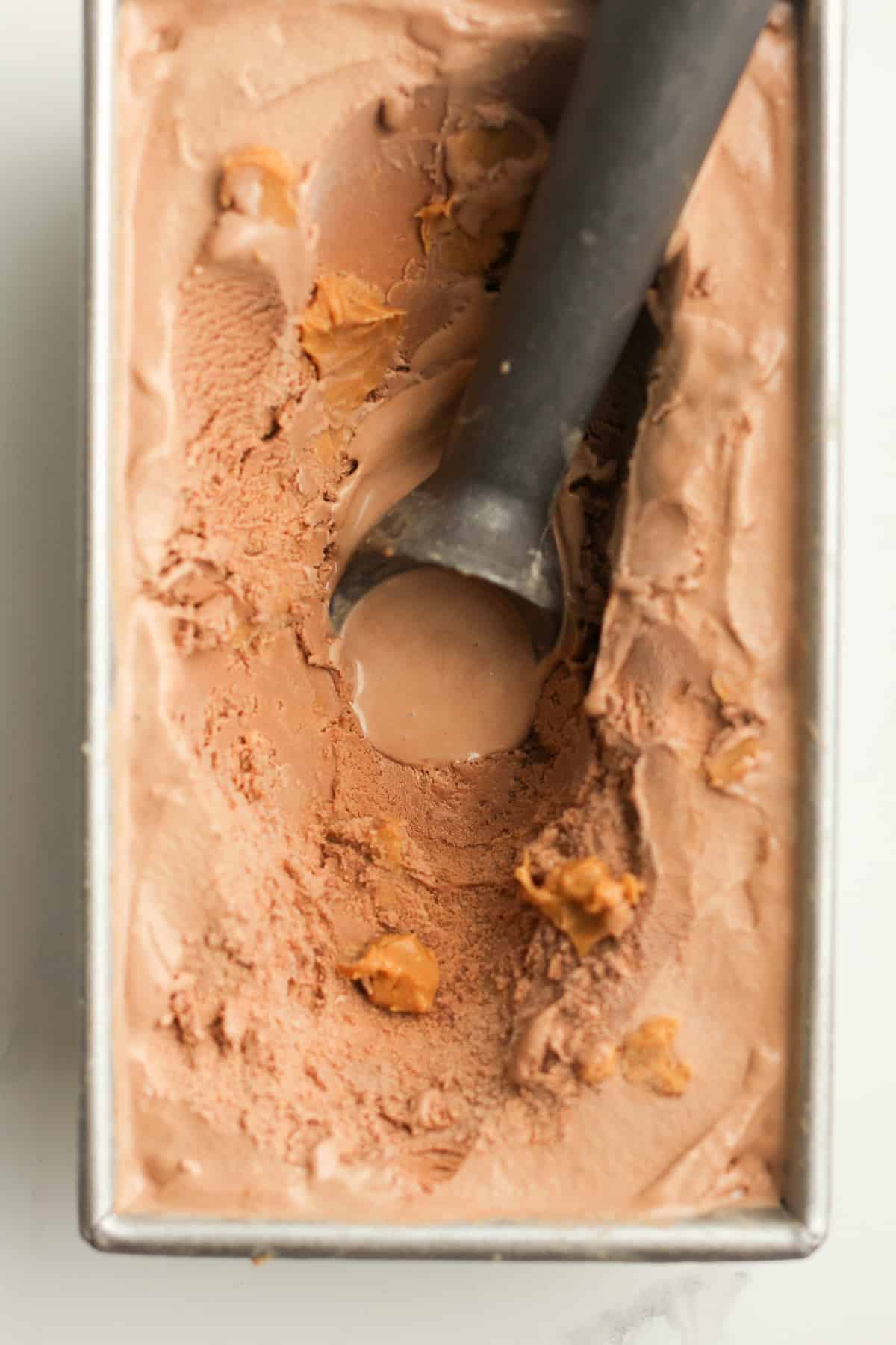 Closeup of a pan of chocolate peanut butter ice cream, with a scooper.