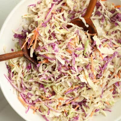 Overhead shot of a white bowl of creamy coleslaw with wooden spoons.