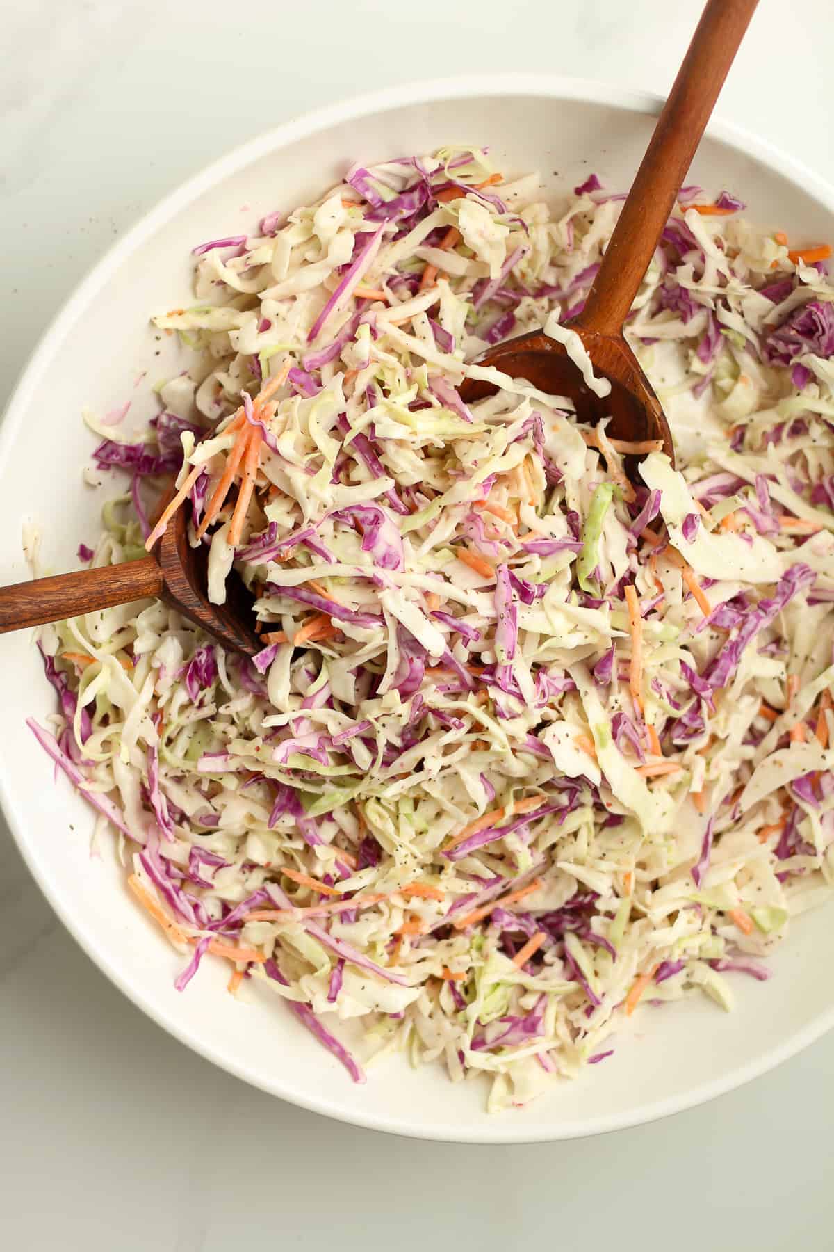 Overhead shot of a white bowl of creamy coleslaw with wooden spoons.