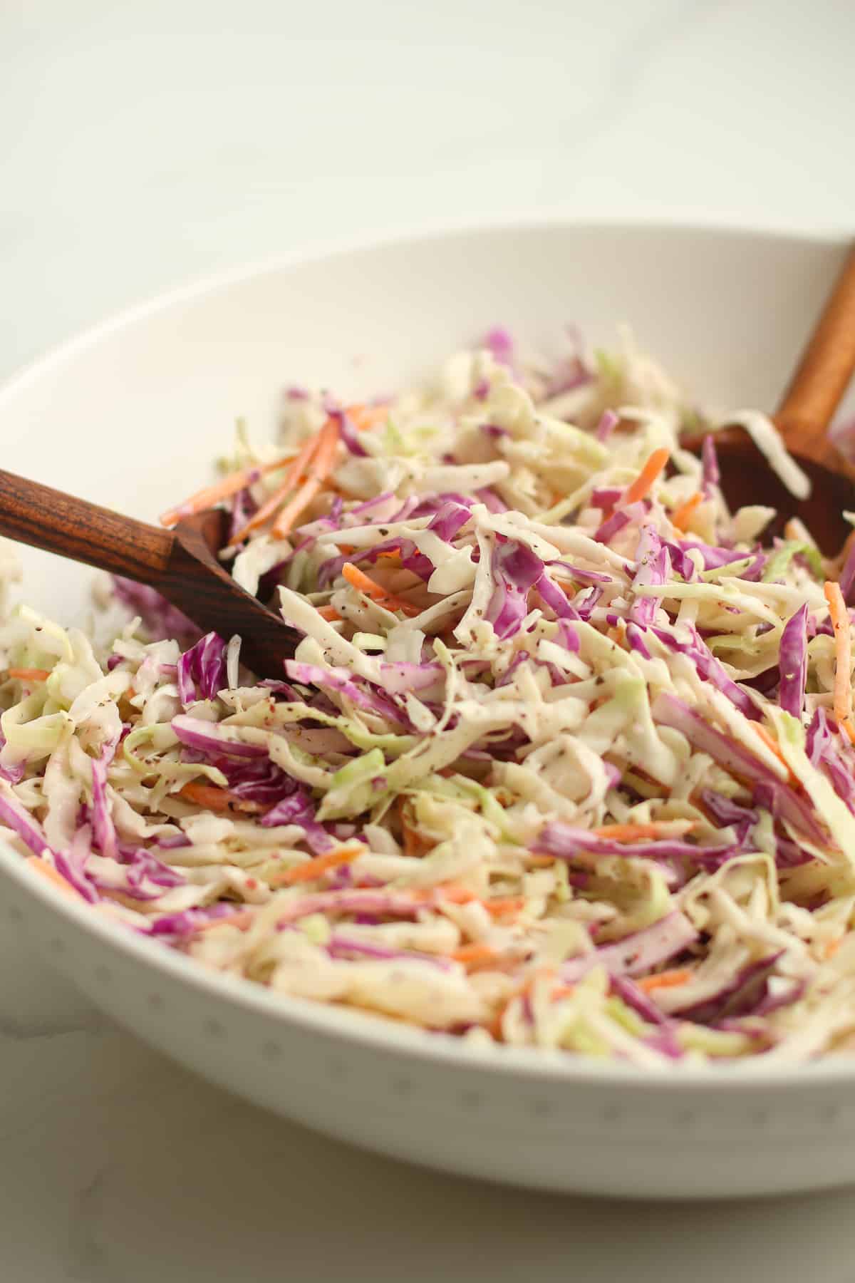 Side shot of a white bowl of creamy coleslaw with wooden spoons.