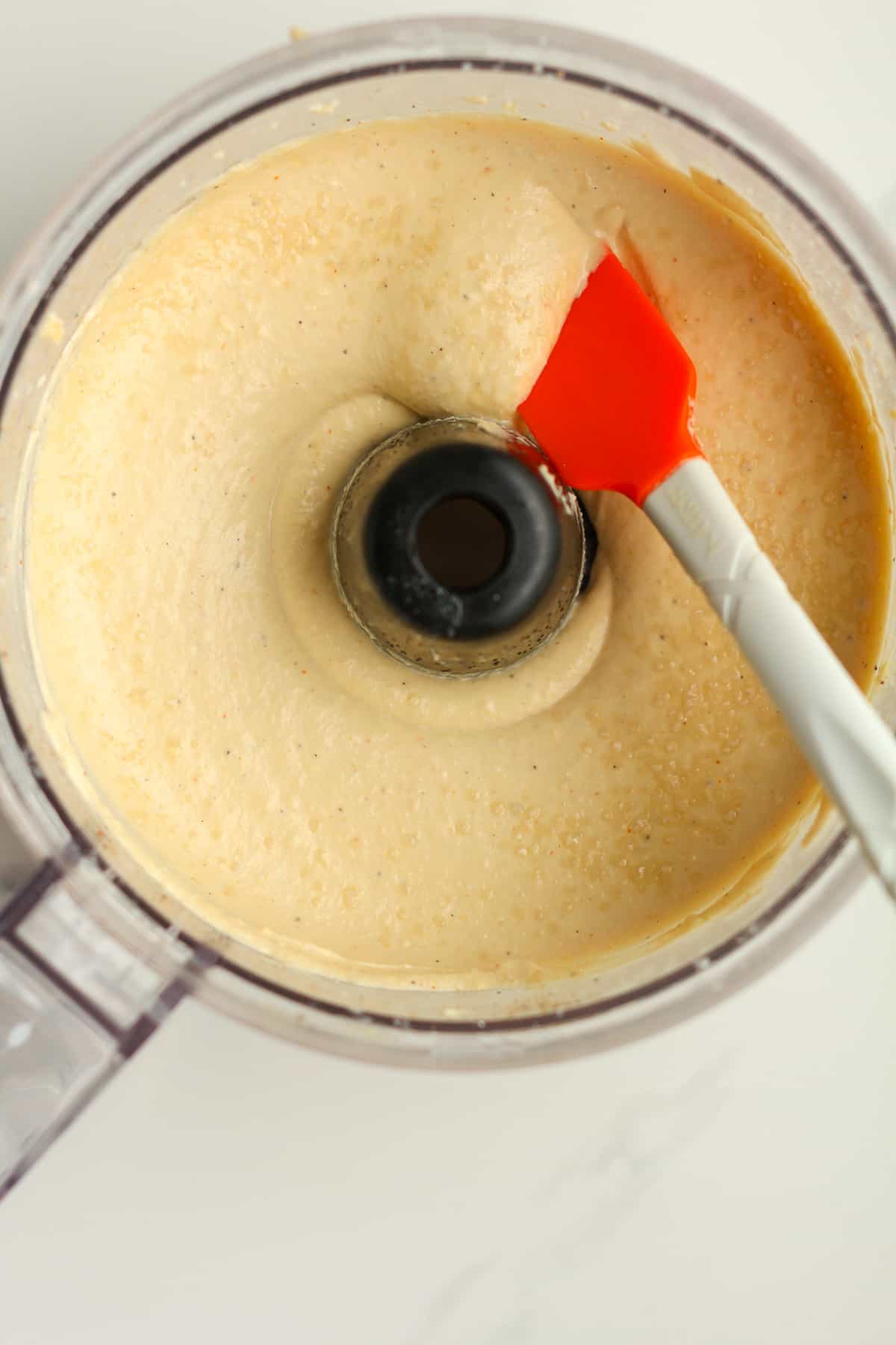 A food processor with a spatula dipped into the hummus.