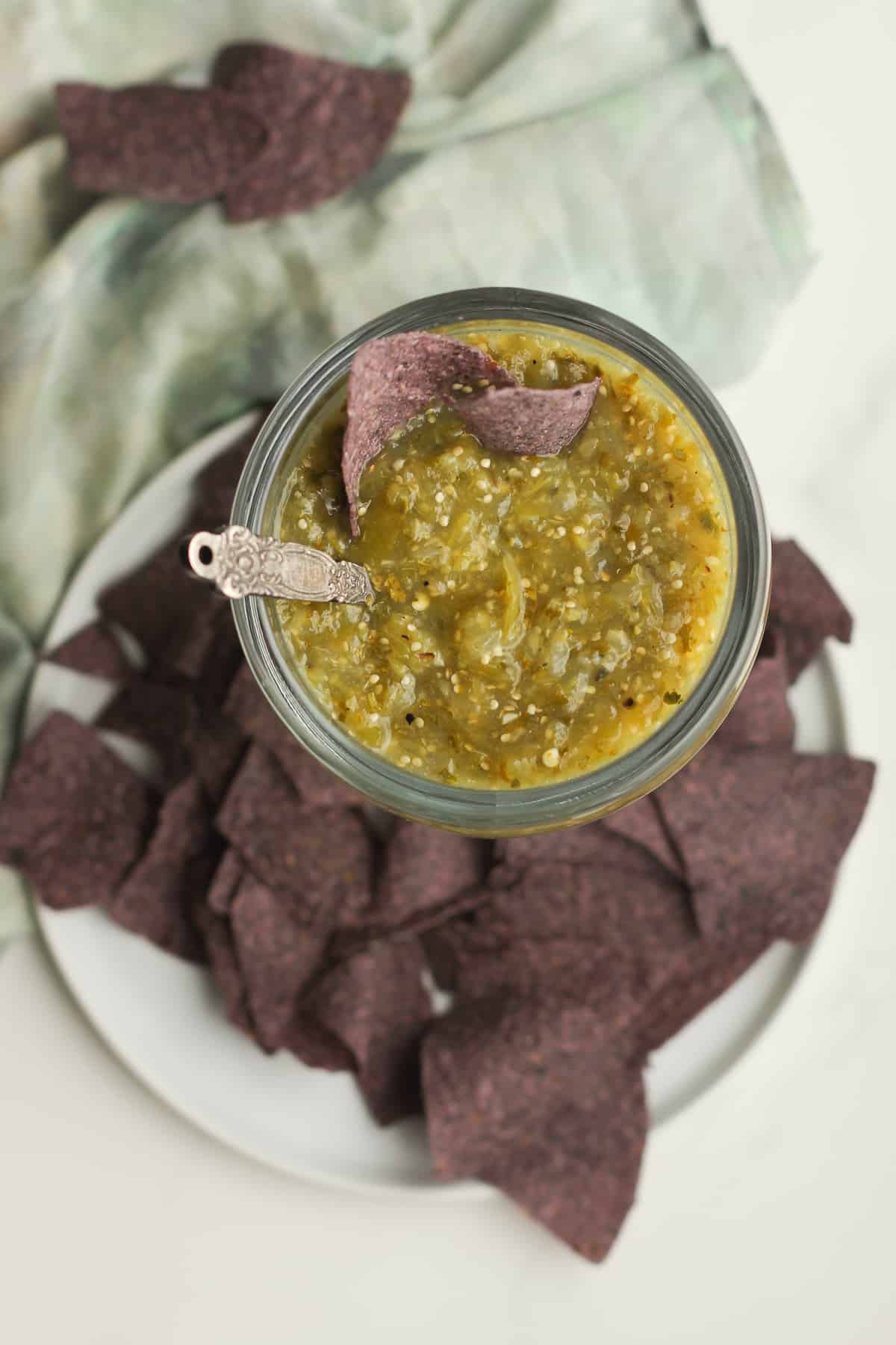 A glass mug of salsa verde, with blue chips.