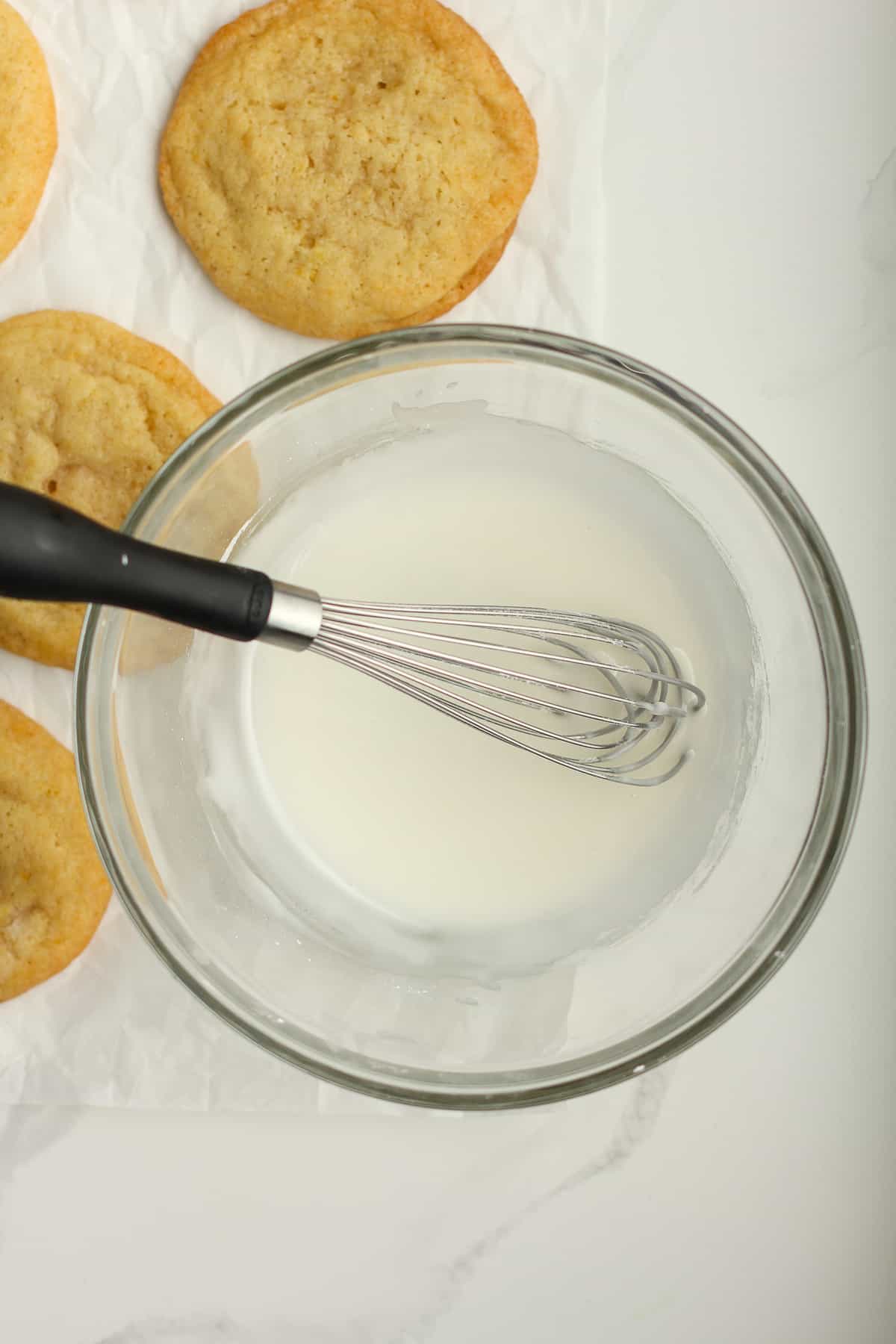 A bowl of glaze next to lemon cookies.