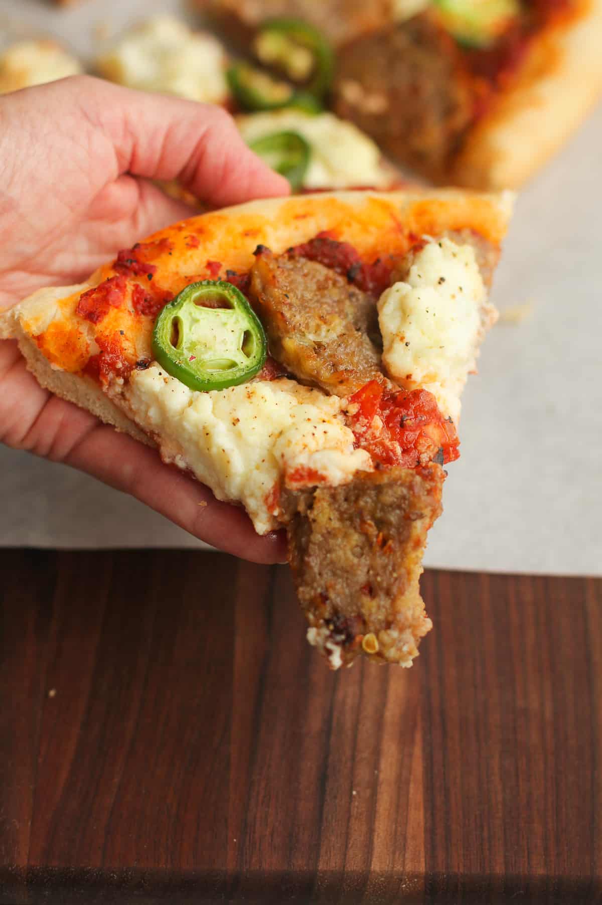 A hand holding a slice of meatball pizza.