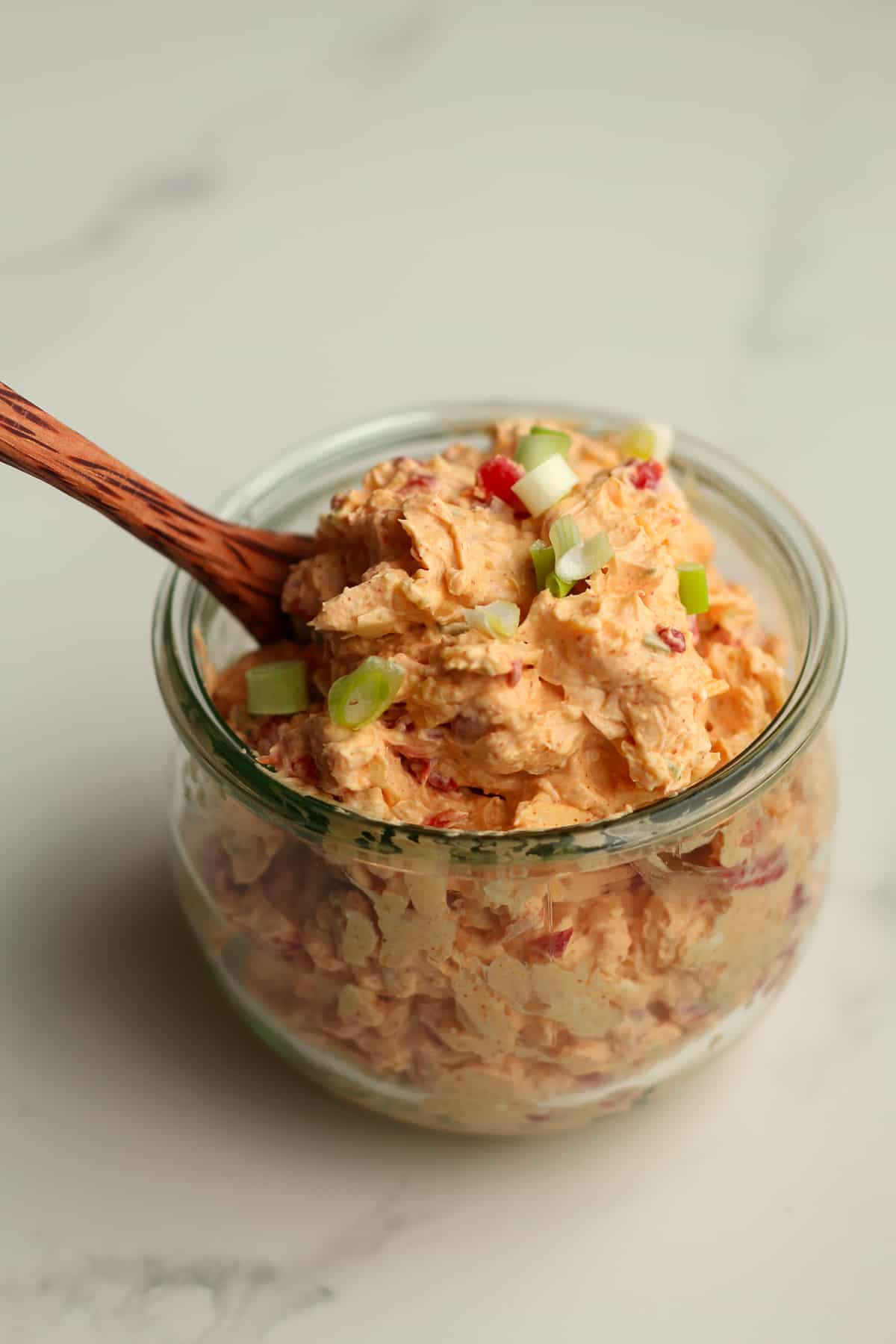 Side shot of a jar of pimento cheese, with a spoon.