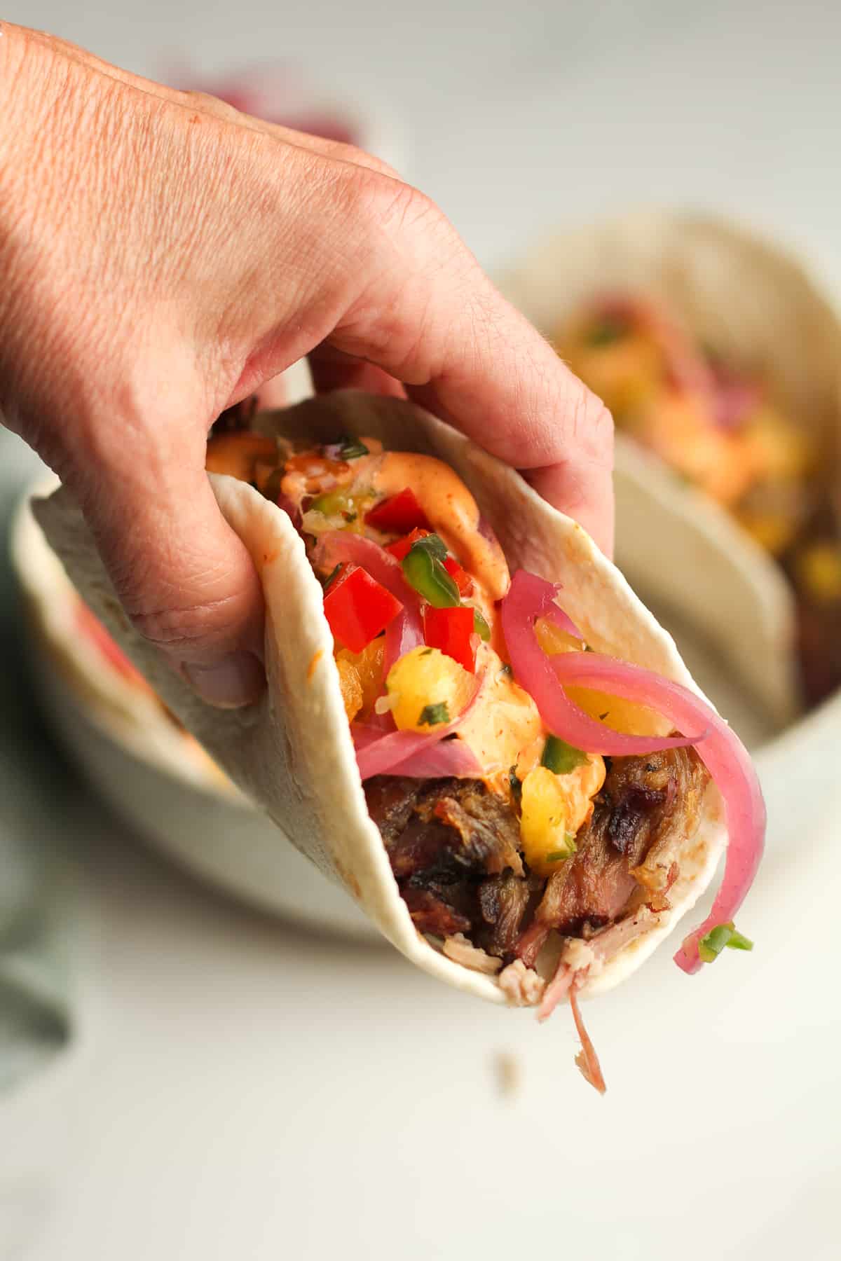 A hand holding a pork taco with pineapple salsa.