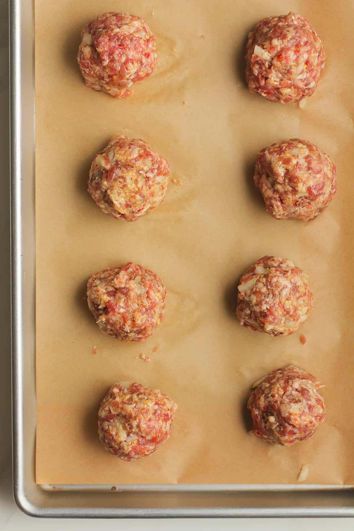 8 raw sausage meatballs on a baking tray.
