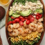 A wooden bowl of a shrimp avocado salad with feta, tomatoes, and corn.