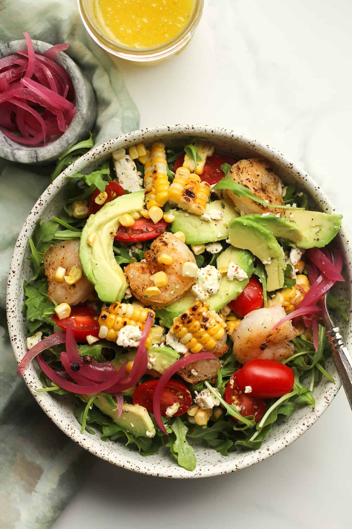 A bowl of avocado shrimp salad with grilled corn and pickled red onions.