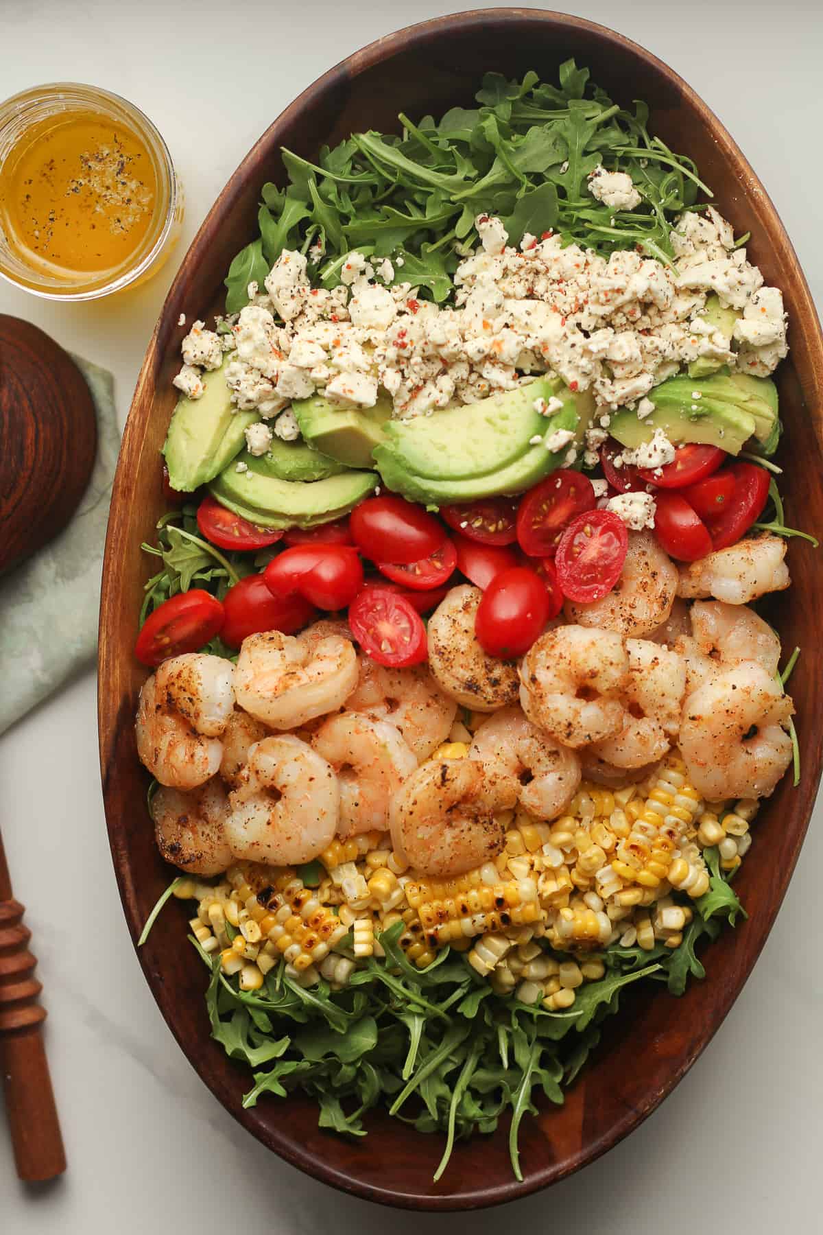 A wooden bowl of a shrimp avocado salad with feta, tomatoes, and corn.