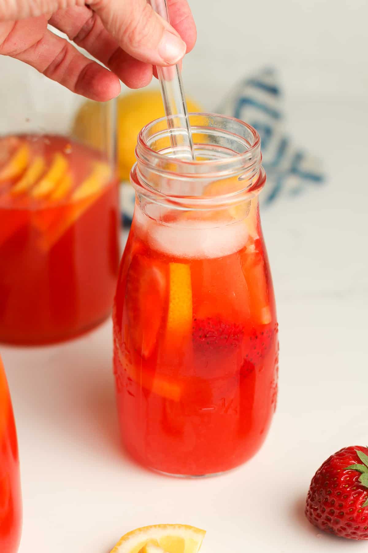 A strawberry vodka lemonade with a hand on the straw.