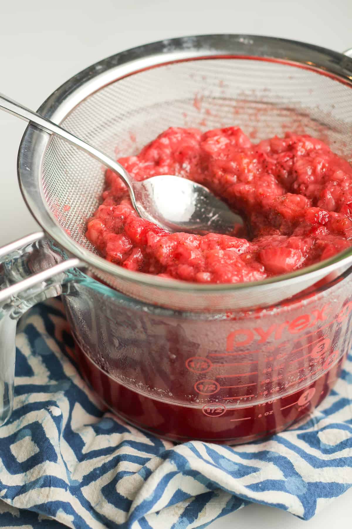 Strawberries in a fine mesh strainer over a measuring cup.