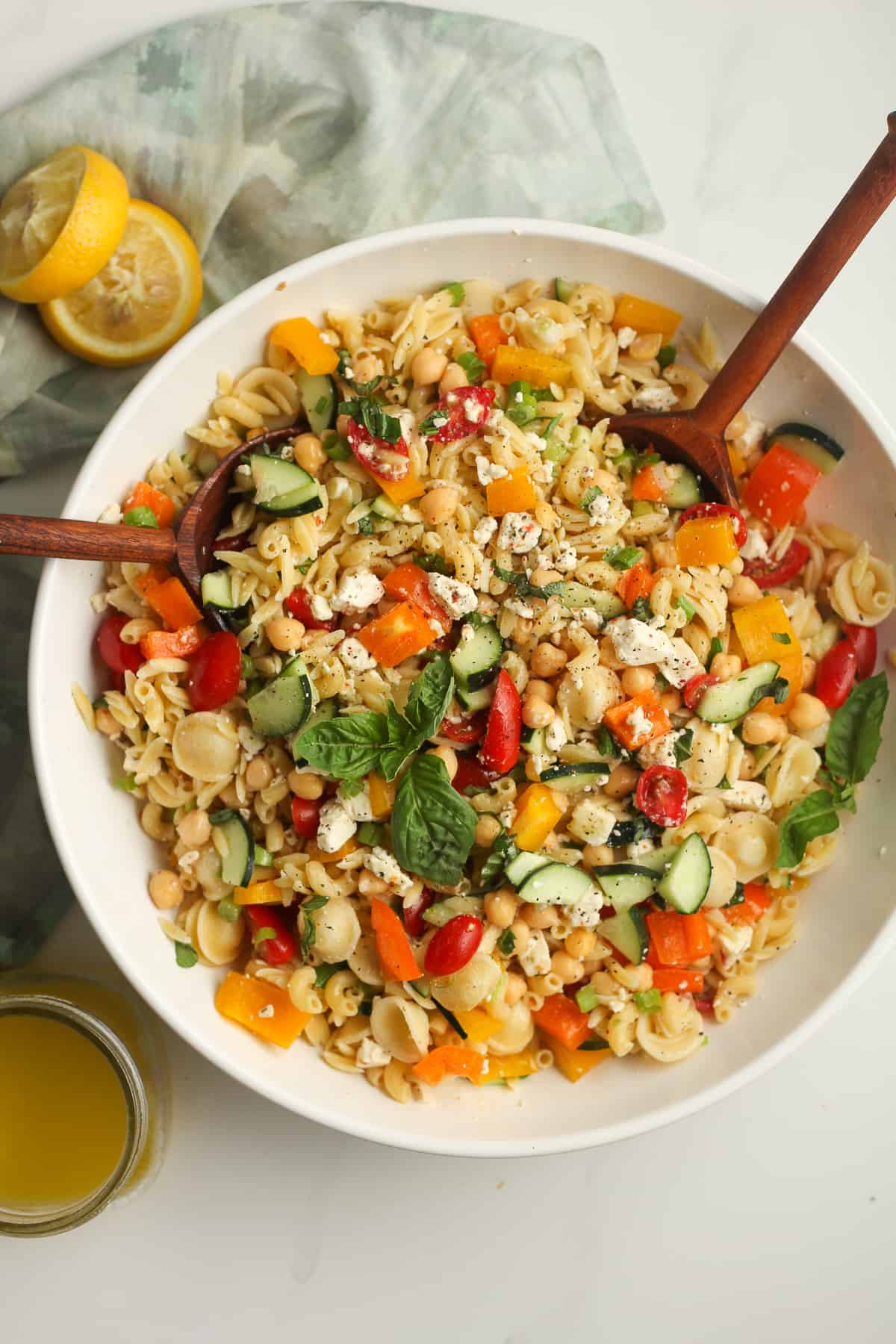 Overhead shot of a large bowl of summer pasta salad with wooden spoons.