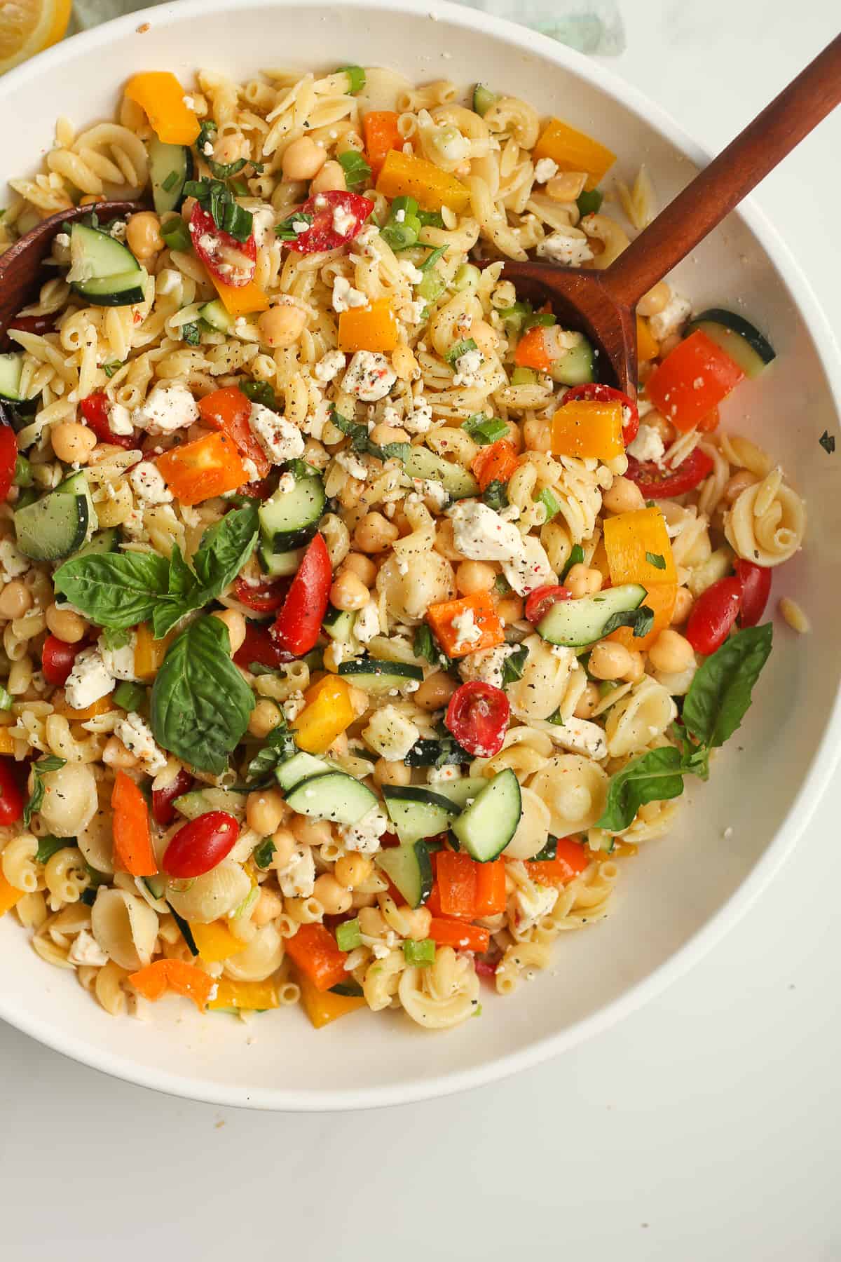 A bowl of summer pasta with two wooden spoons.