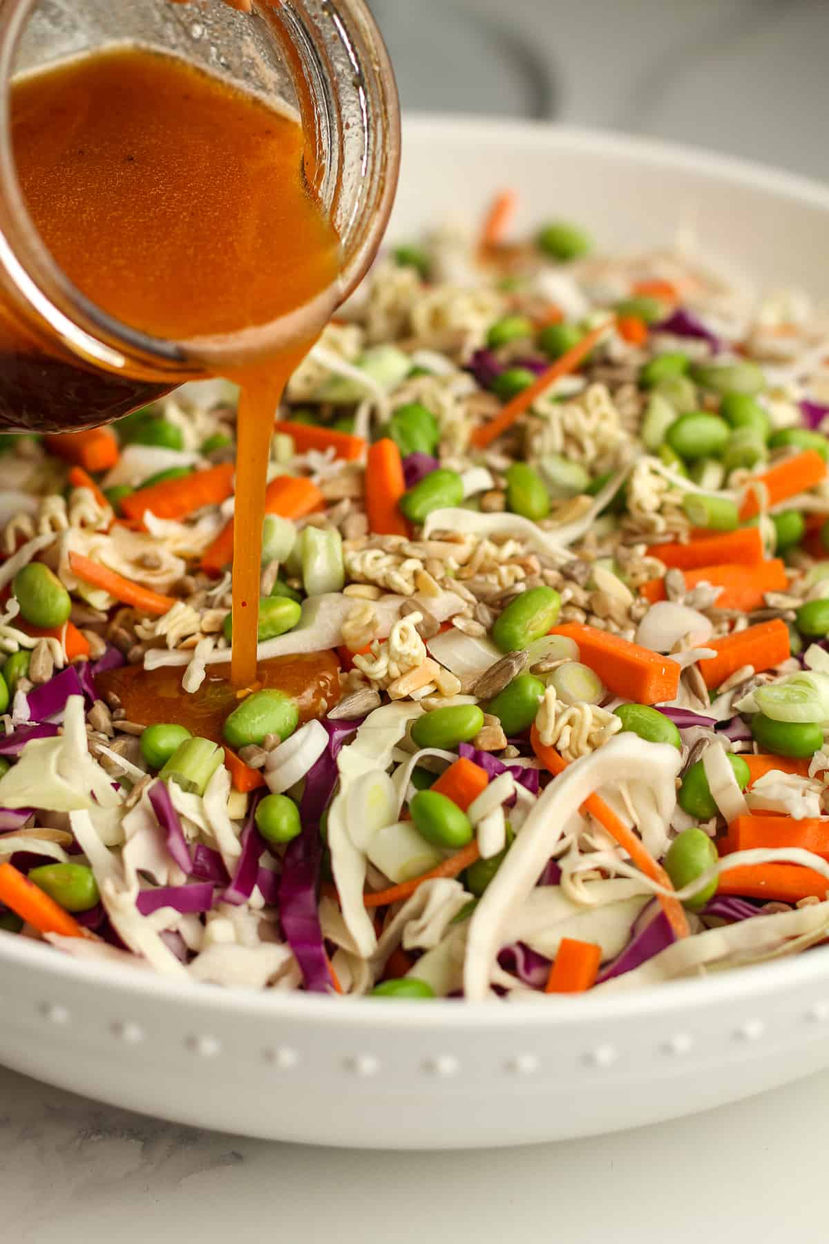 A jar of dressing being poured on the salad.