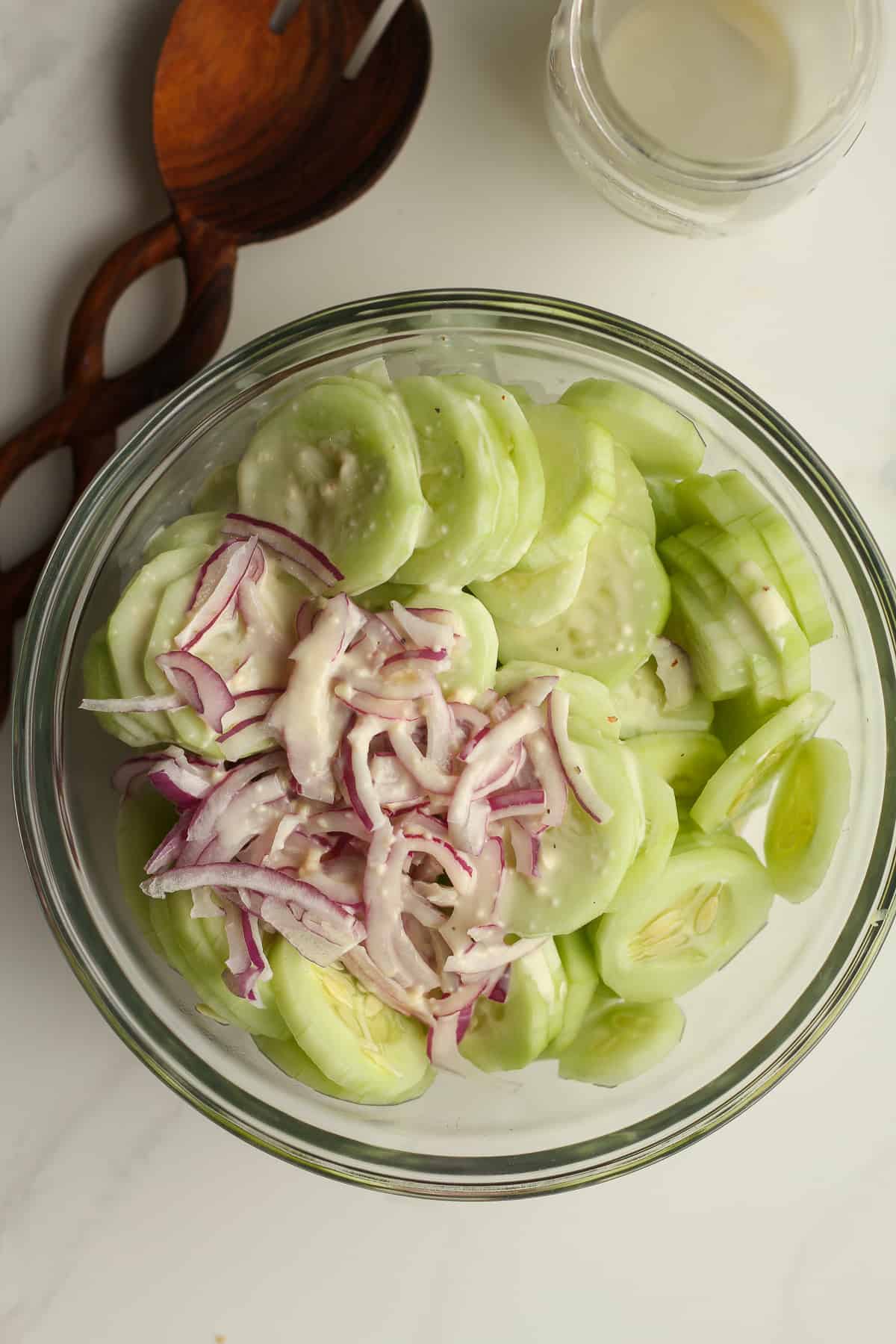A bowl of sliced cucumbers and red onions, with the dressing on top.