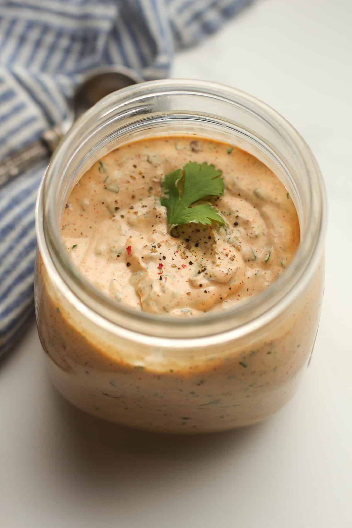 A jar of chipotle ranch, with a sprig of cilantro.