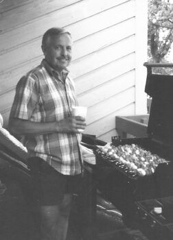 My dad grilling some kabobs with a drink in his hand.